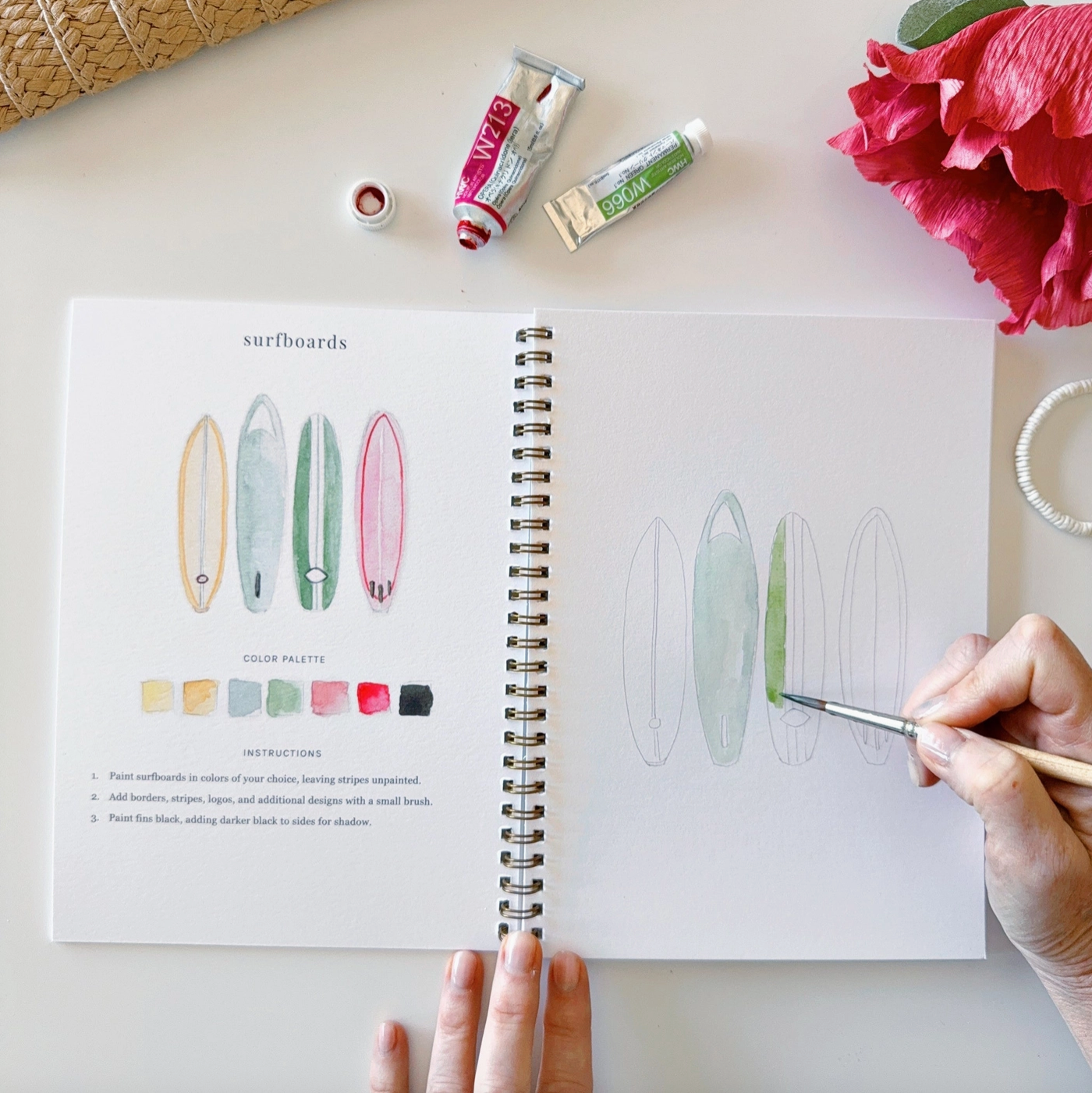The open watercolor book with an image of surfboards and instructions to paint them.