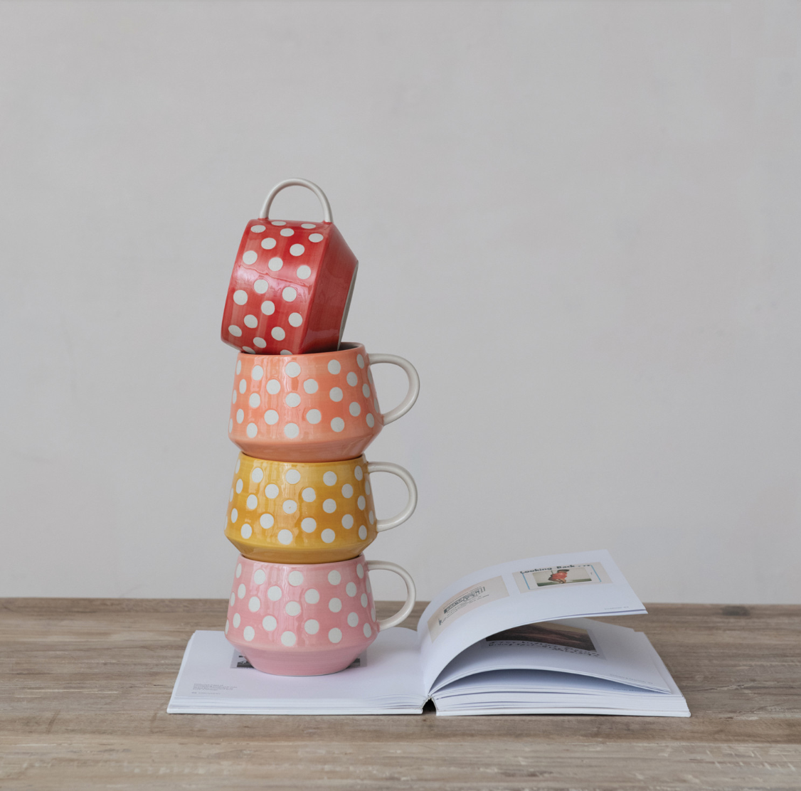 Stack of colorful polka dot mugs on an open book with a plain background