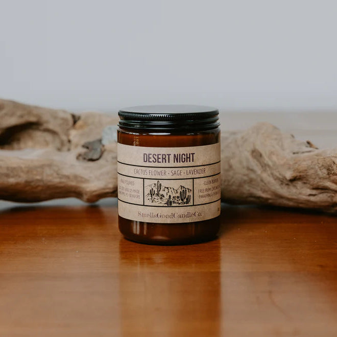 A soy wax candle jar with a label that reads 'Desert Night', placed on a wooden surface with a piece of driftwood in the background.