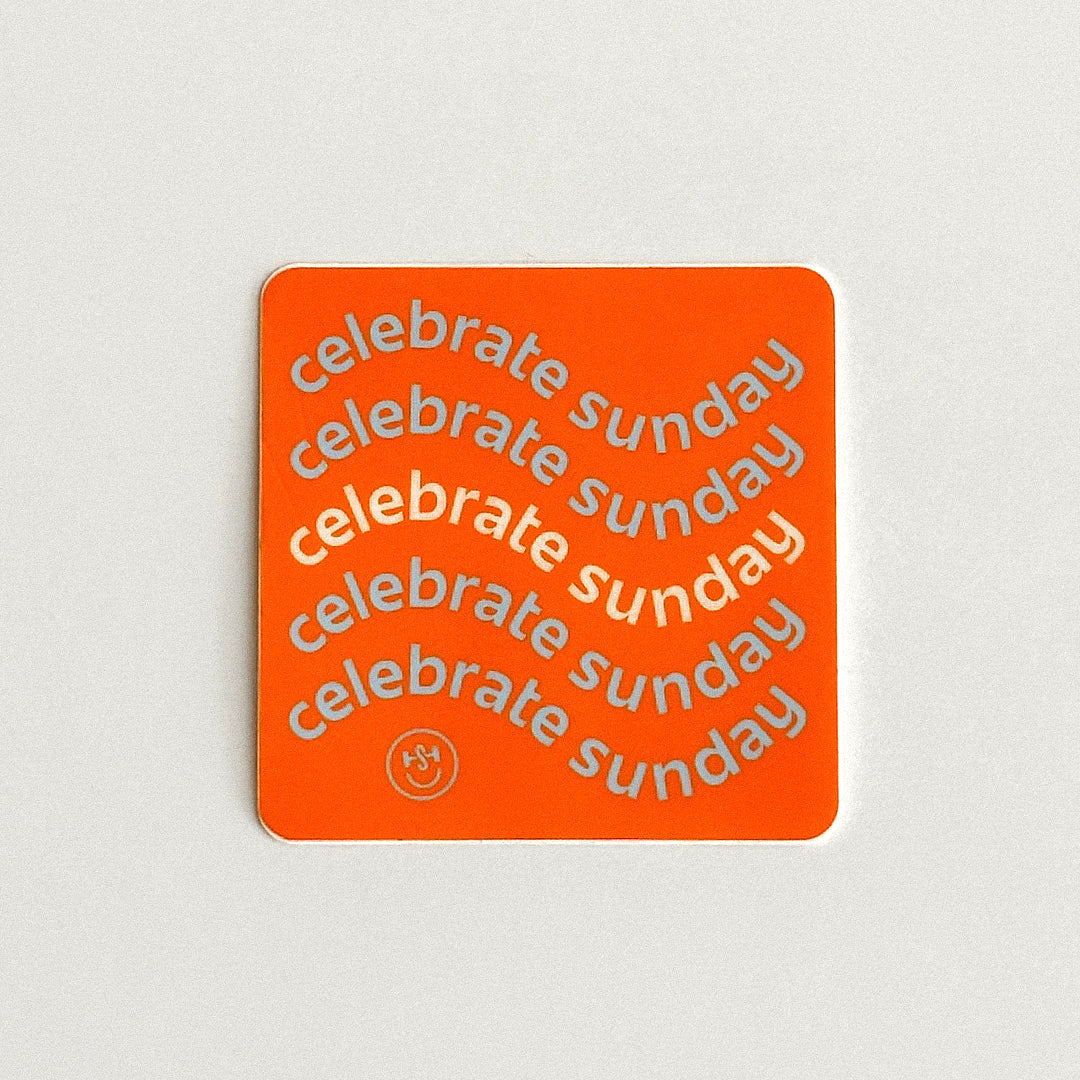 An orange square sticker with rounded corners features the phrase “celebrate Sunday” repeated diagonally in white and light blue lettering. A small circular smiley logo appears near the bottom of the sticker.