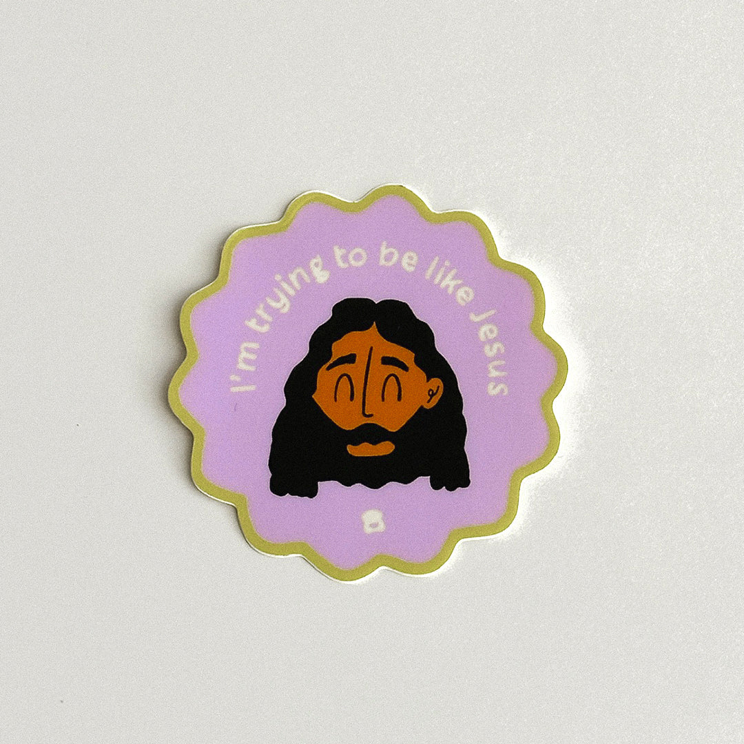 A purple scalloped sticker features a playful illustration of Jesus with dark hair and a beard. White lettering around the illustration reads, “I’m trying to be like Jesus.”