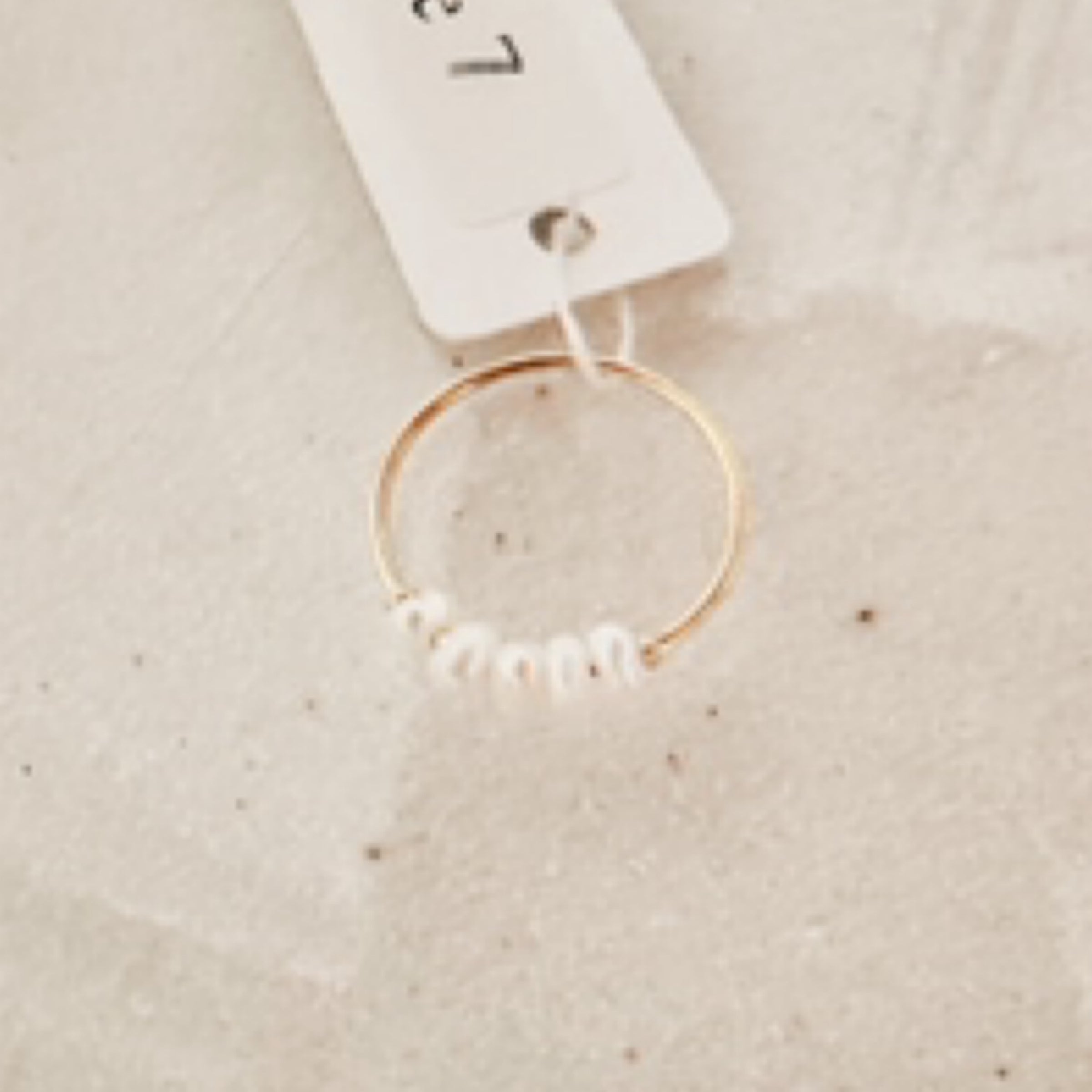 Super thin gold band with 5 white pearls clustered along the top. Pictured against white sand.