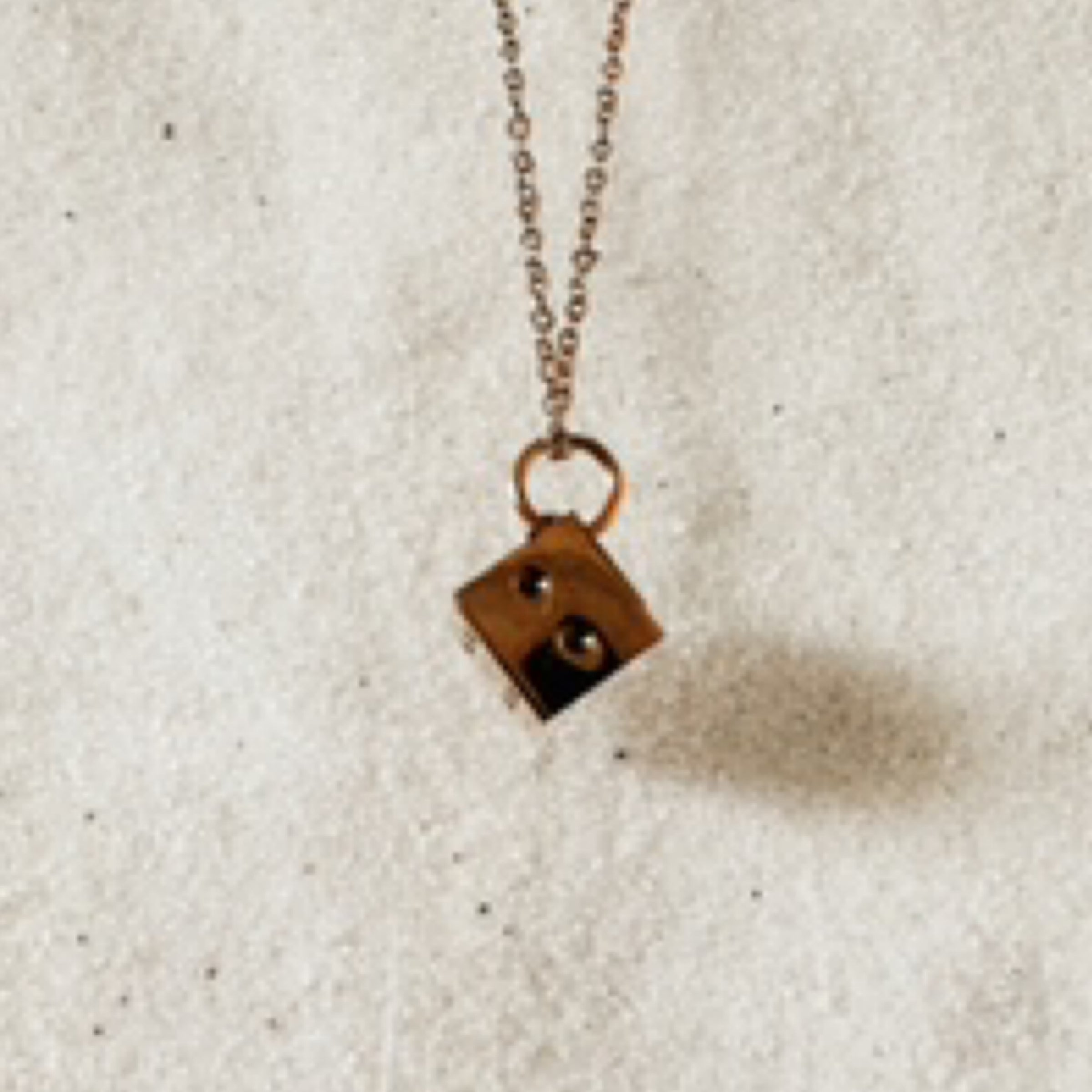 Delicate gold chain with a life like gold die pendant. Pictured against white sand.