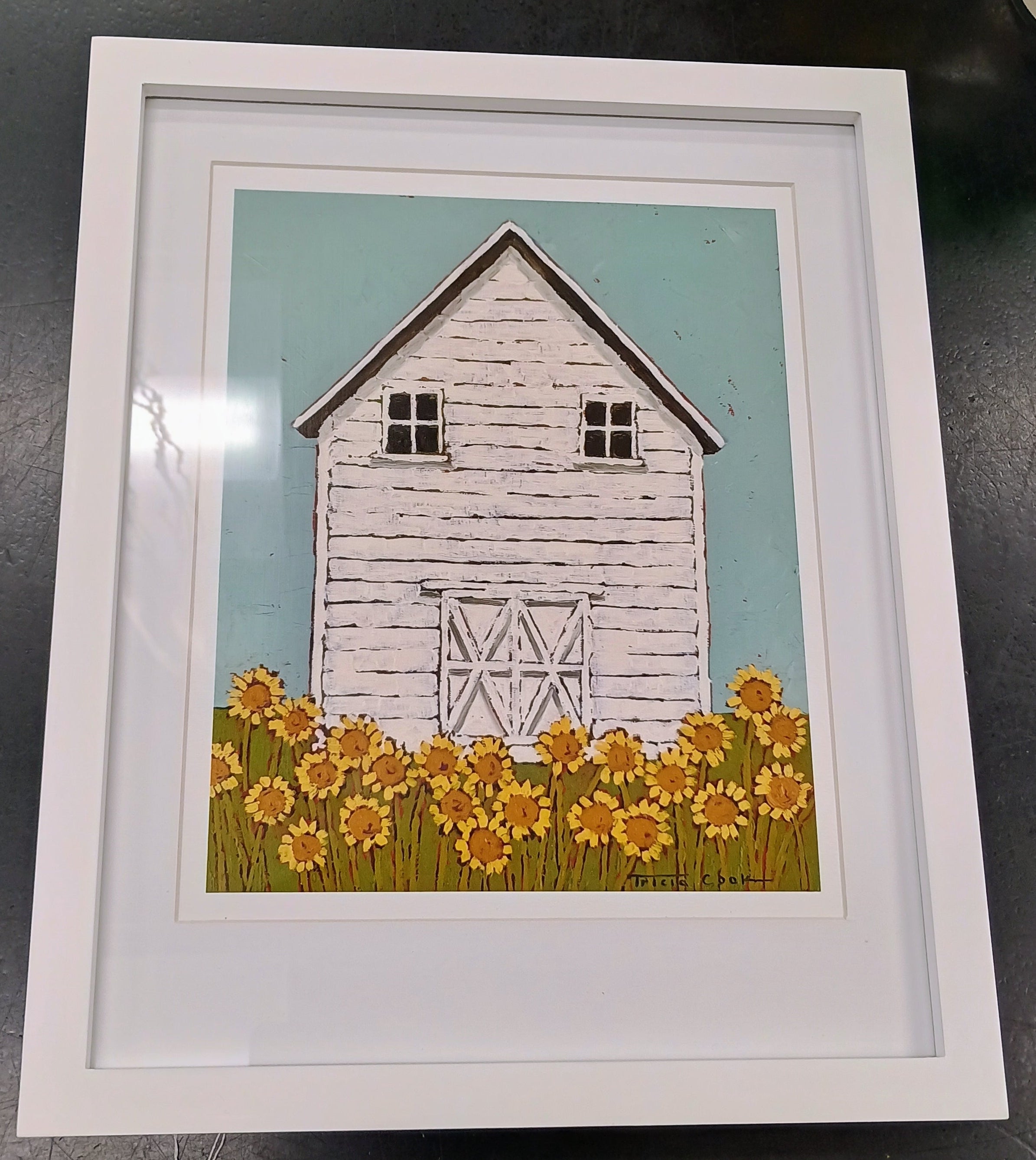 Framed print of rustice white barn, with ligth blue sky, and yellow sunflowers in the foreground.