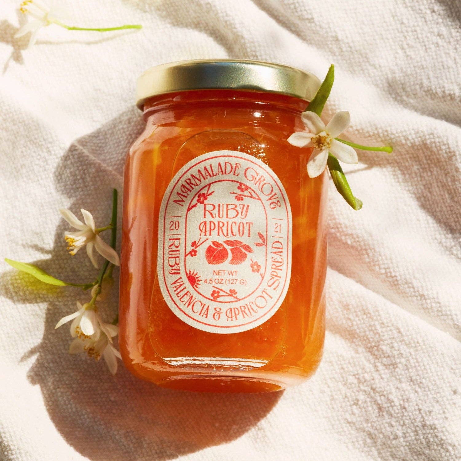 Jar of ruby apricot marmalade with a decorative label on a light fabric background