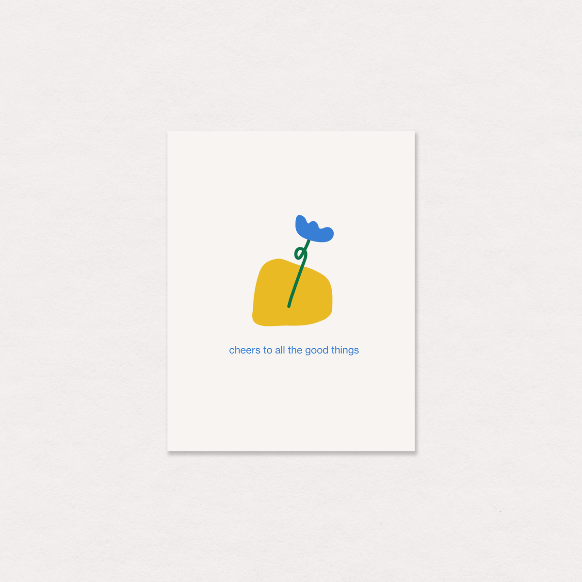 A minimalist art print greeting card featuring a yellow abstract shape with a blue flower and green stem, and the text 'cheers to all the good things' below, displayed on a textured off-white background.