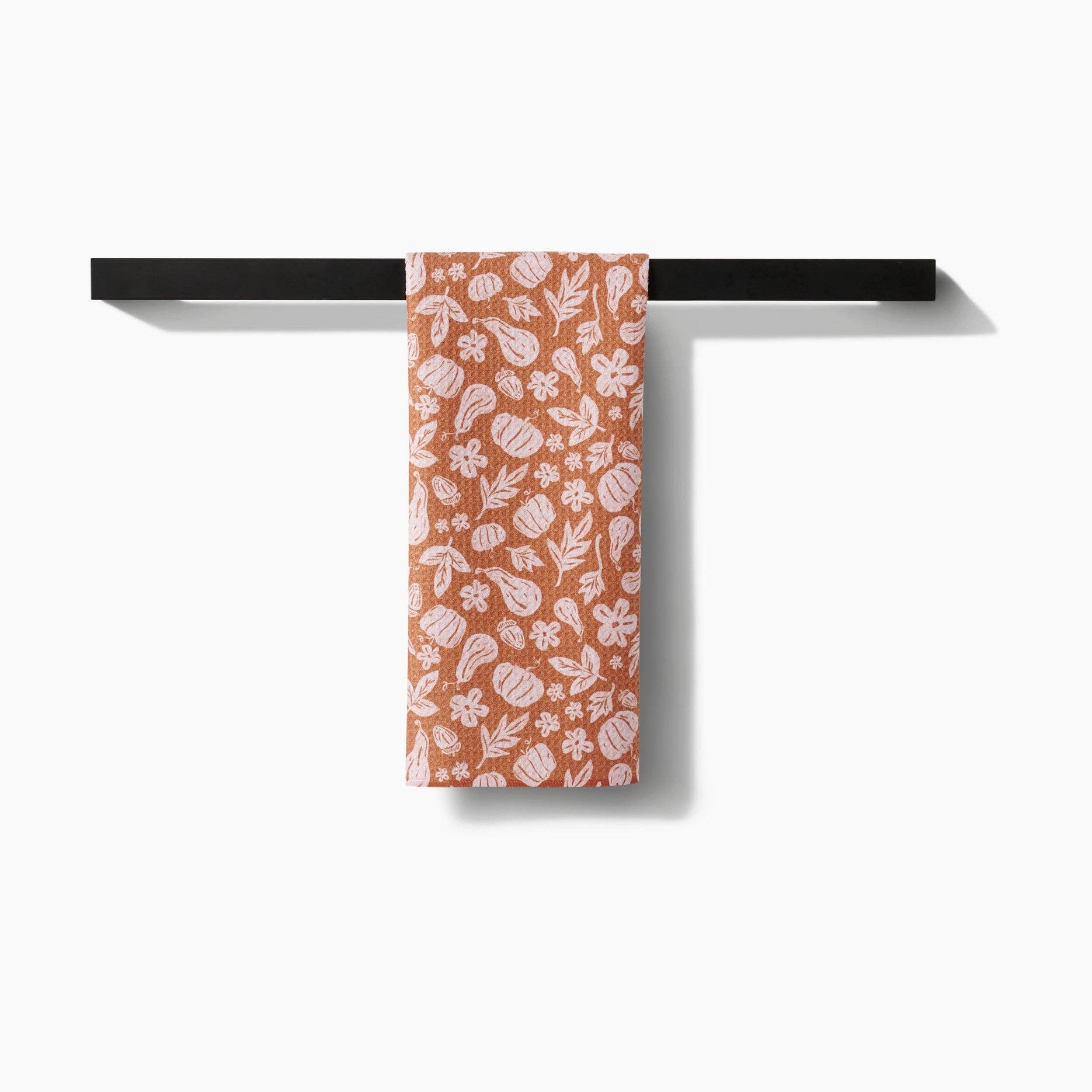 Towel with pumpkin and leaf pattern hanging on a black towel rack against a white background