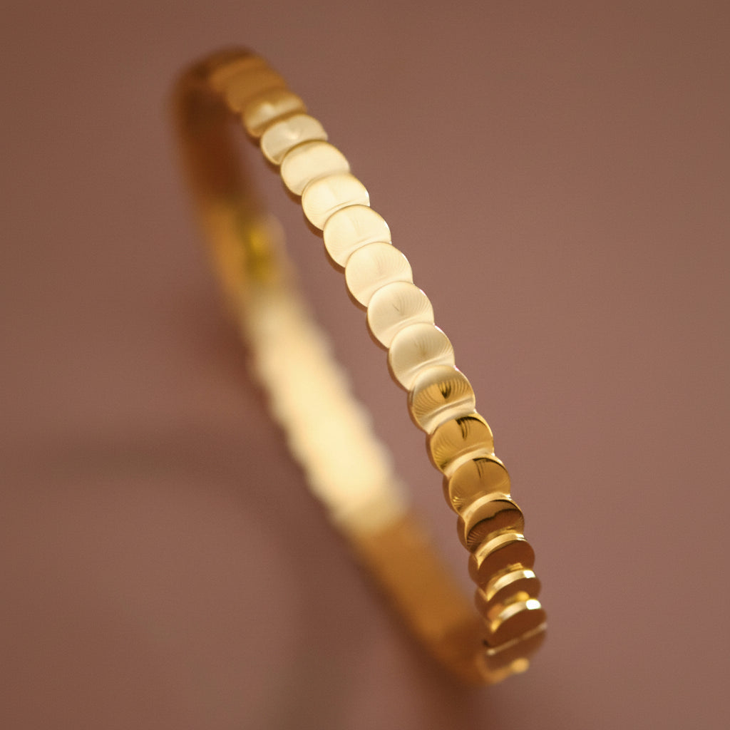 Elegant 18K gold plated stainless steel hinged bangle bracelet featuring delicate layered circles. With an inner oval diameter of 2.36" and 7" circumference, this piece offers a comfortable, versatile fit. Hypoallergenic, waterproof, and tarnish-resistant, it's designed to withstand daily wear and moisture exposure. The hinged closure makes it easy to slip on and off while maintaining a secure fit. To preserve the lustrous gold finish, avoid prolonged contact with lotions, perfumes, and harsh chemicals.