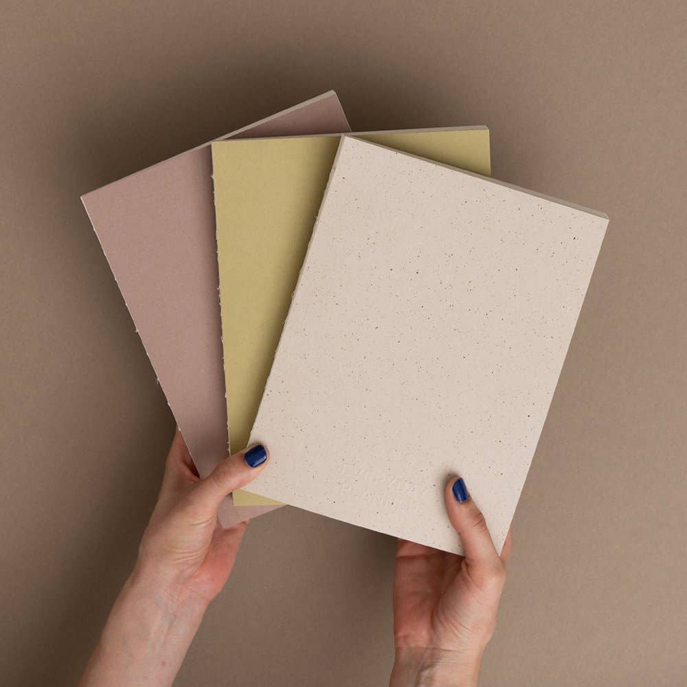 Three notebooks in different colors held by hands against a brown background