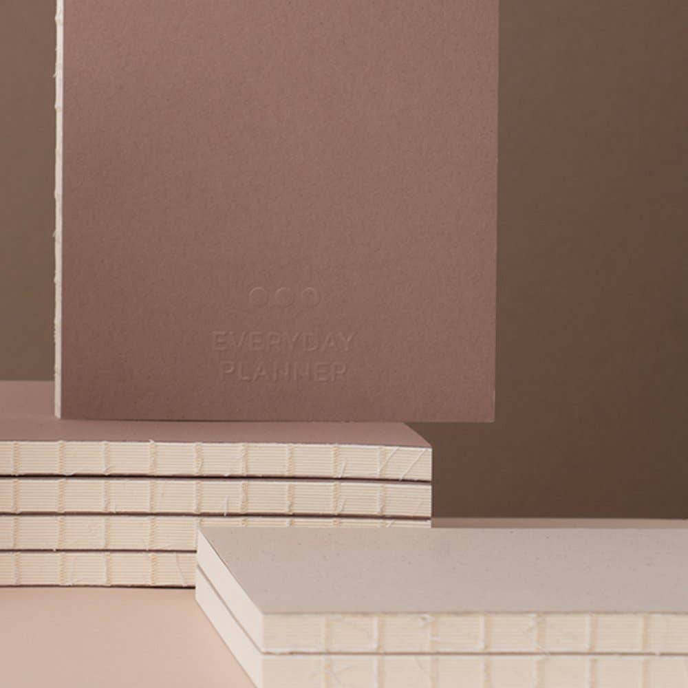 Stack of notebooks with 'Everyday Planner' text on a brown background