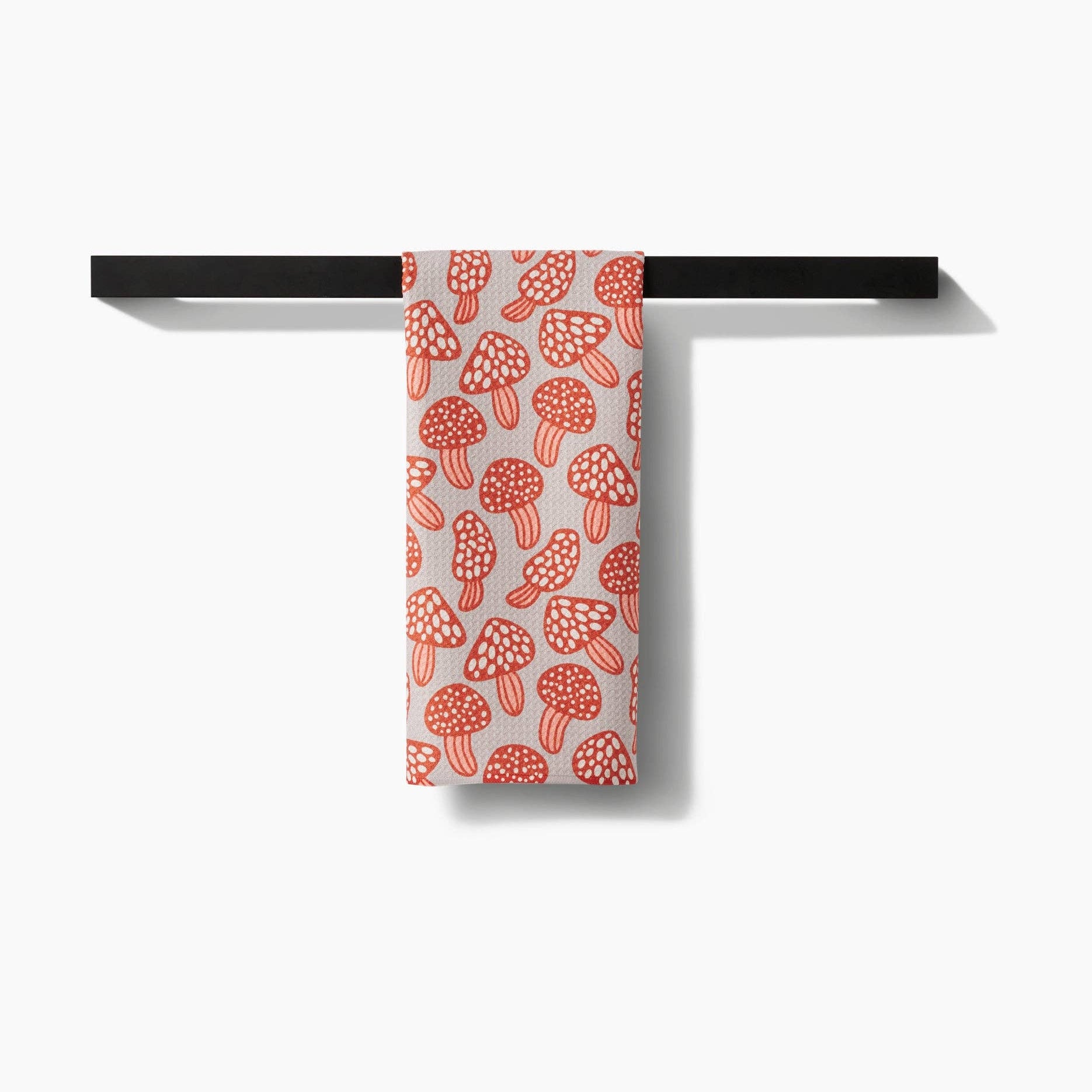 Towel with red mushroom pattern hanging on a black rack against a white background