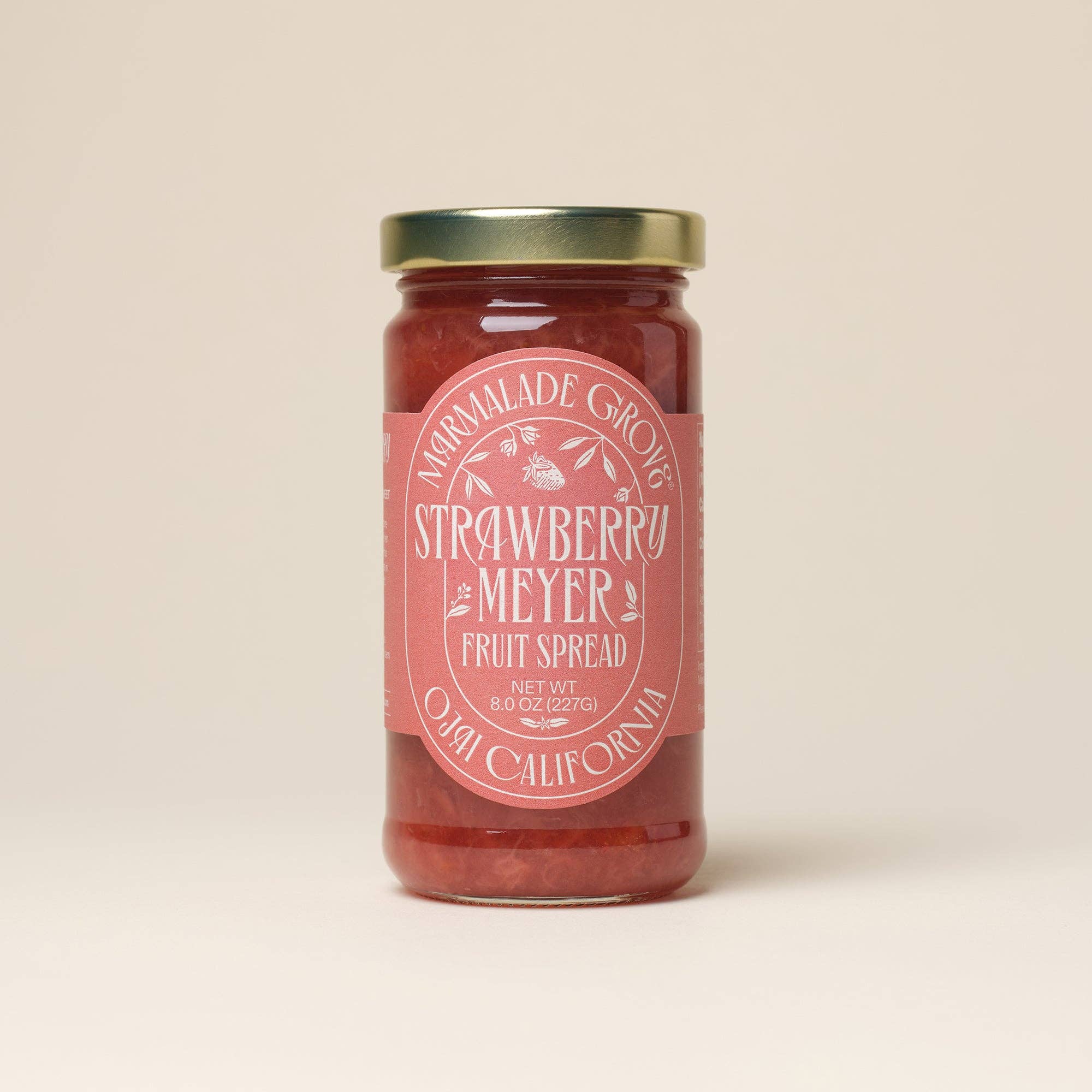 A glass jar of Normalade Grove Strawberry Meyer Fruit Spread with a dusty pink label and a gold metal lid, set against a solid light beige background.