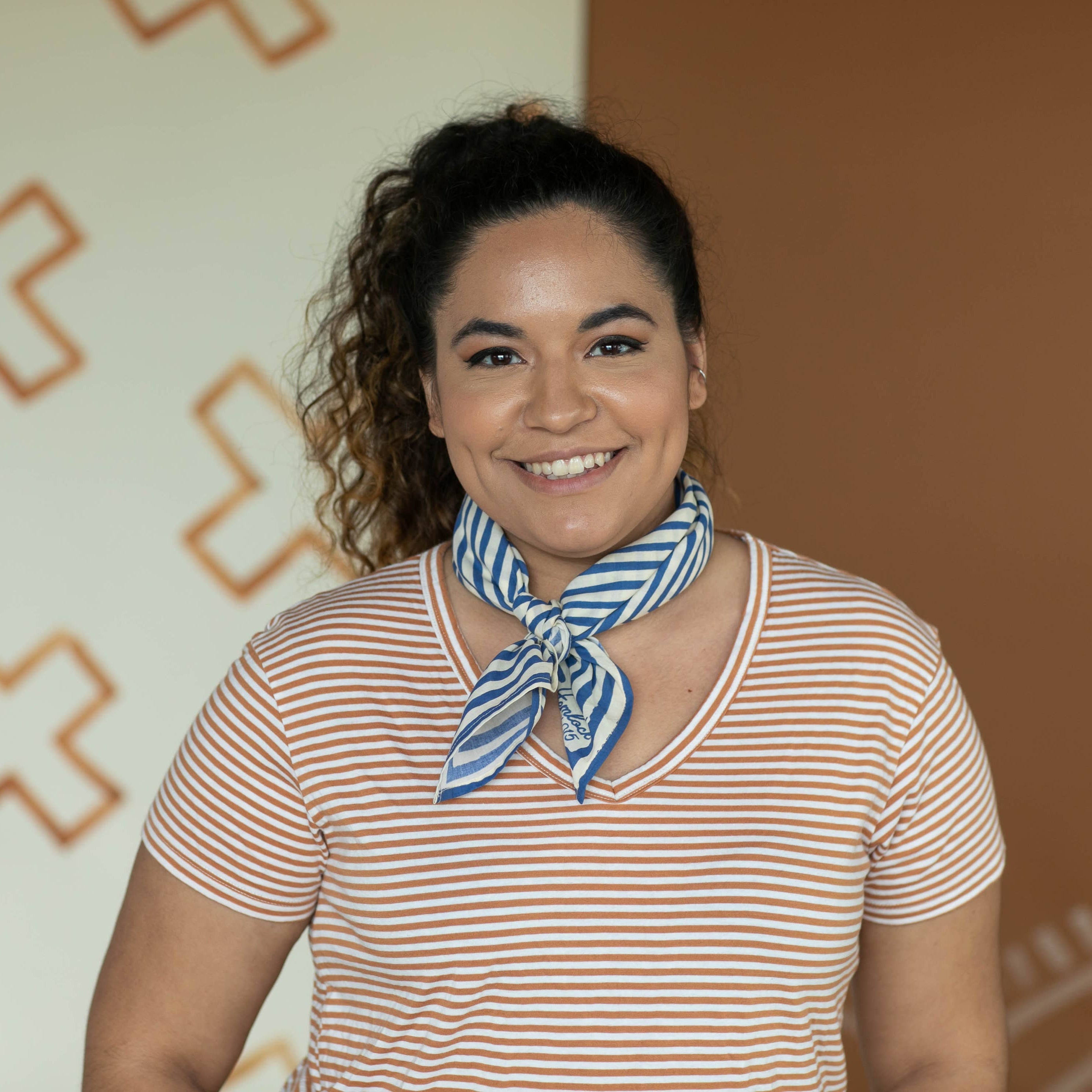 Woman wearing a striped shirt and blue scarf against a decorative wall.