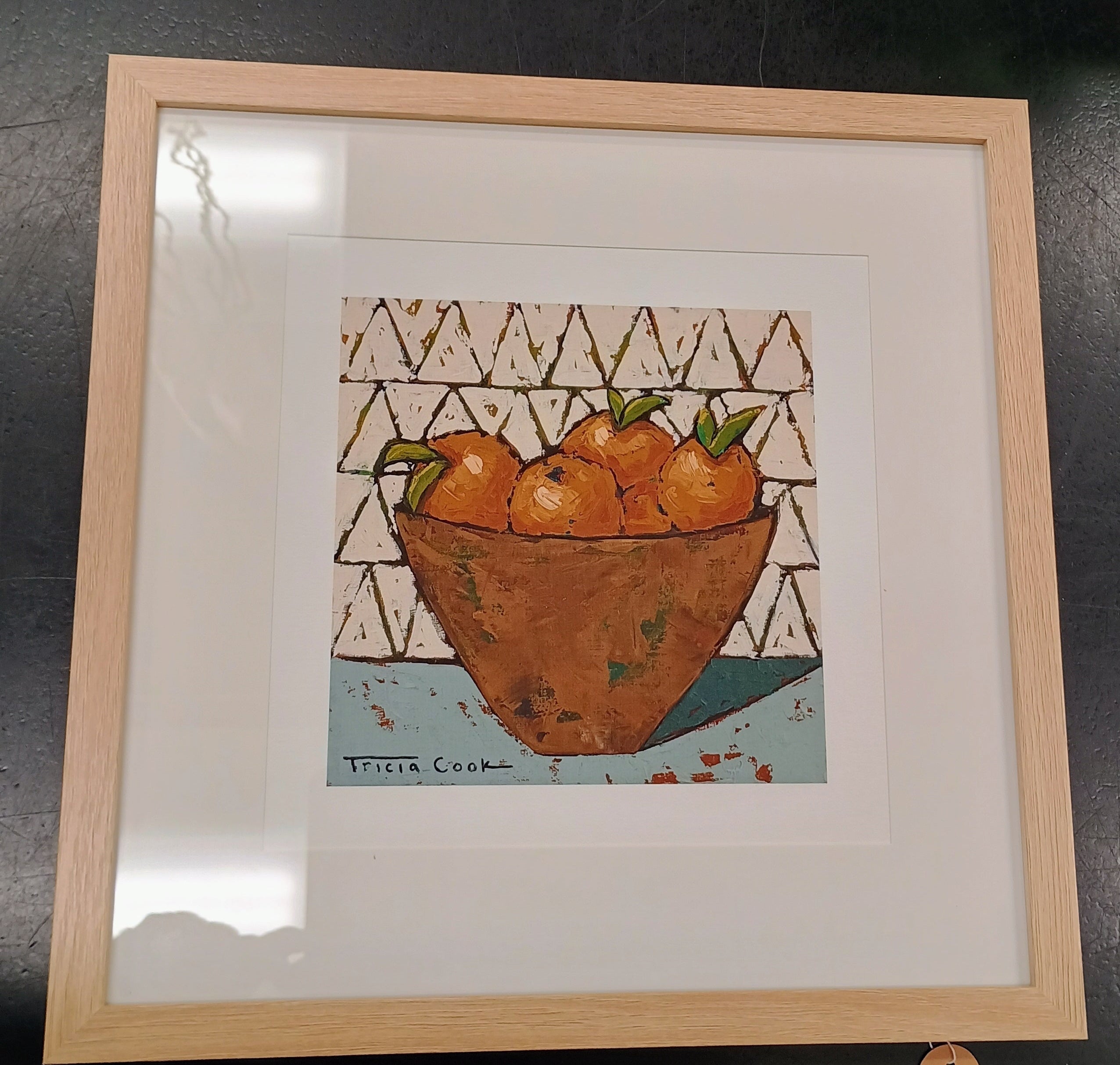 Framed Print with rust colored bowl of clementines on a light blue tabletop with a white tile wall. Frame is thin natural wood with wide white mat board