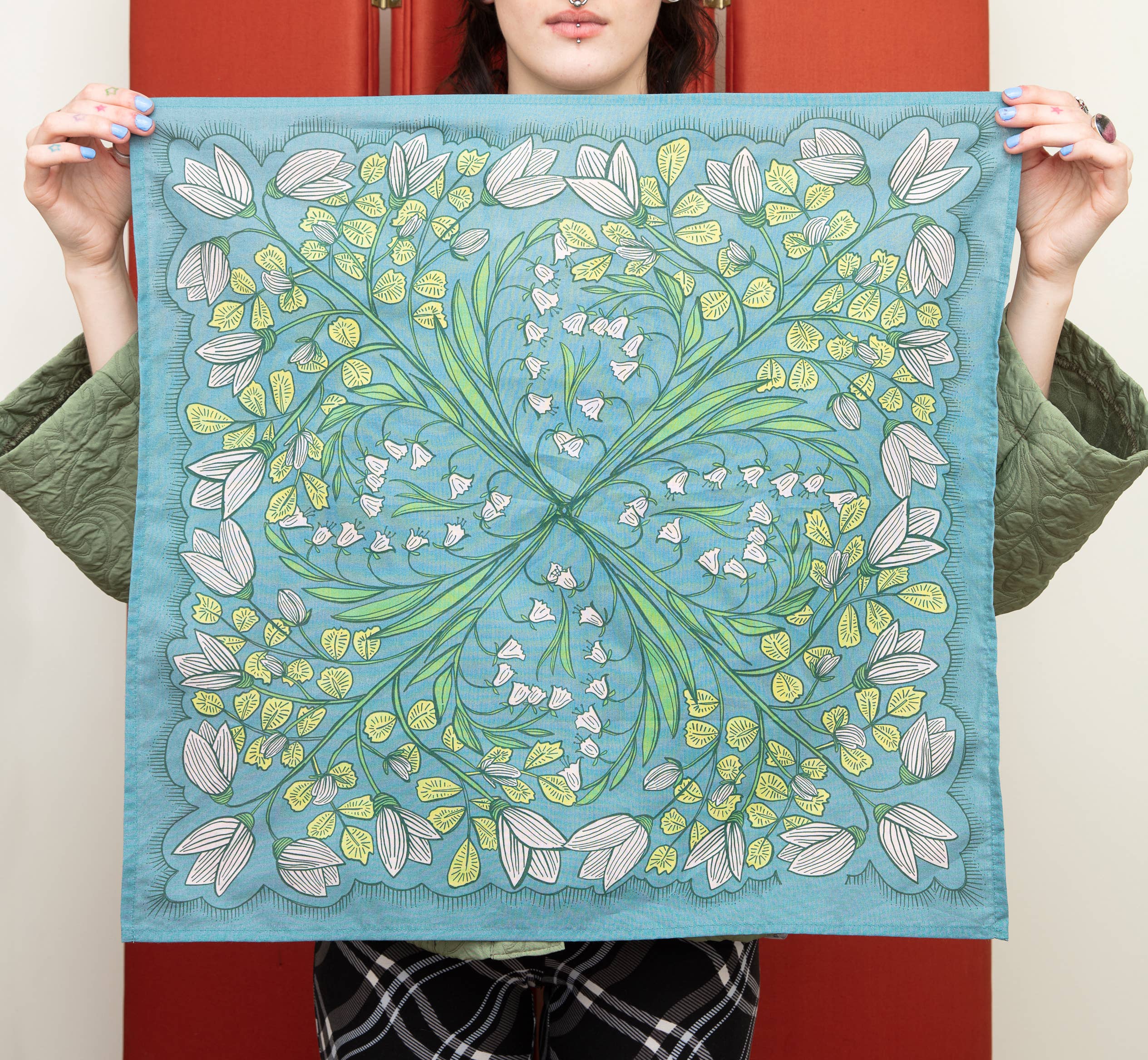Person holding a square piece of fabric with a floral pattern against a red background