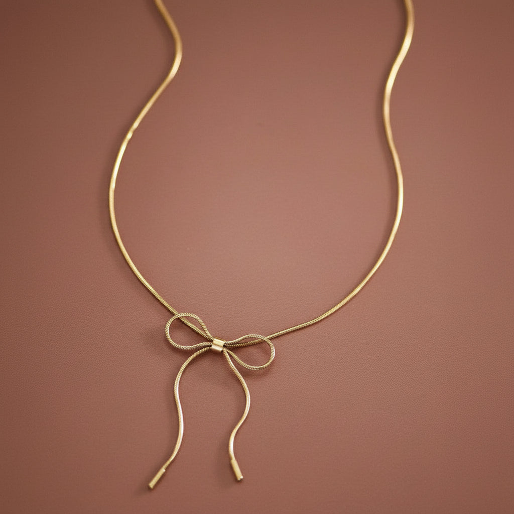 Elevate your everyday style with this delicate dainty bow pendant necklace, crafted from waterproof stainless steel with luxurious 18K gold plating. Hypoallergenic and tarnish-resistant, it's designed for sensitive skin and daily wear. The drapey bow design adds a touch of feminine elegance to any outfit. To maintain its radiant finish, avoid contact with lotions, perfumes, and cleaning products. A versatile piece that effortlessly transitions from casual to sophisticated occasions.
