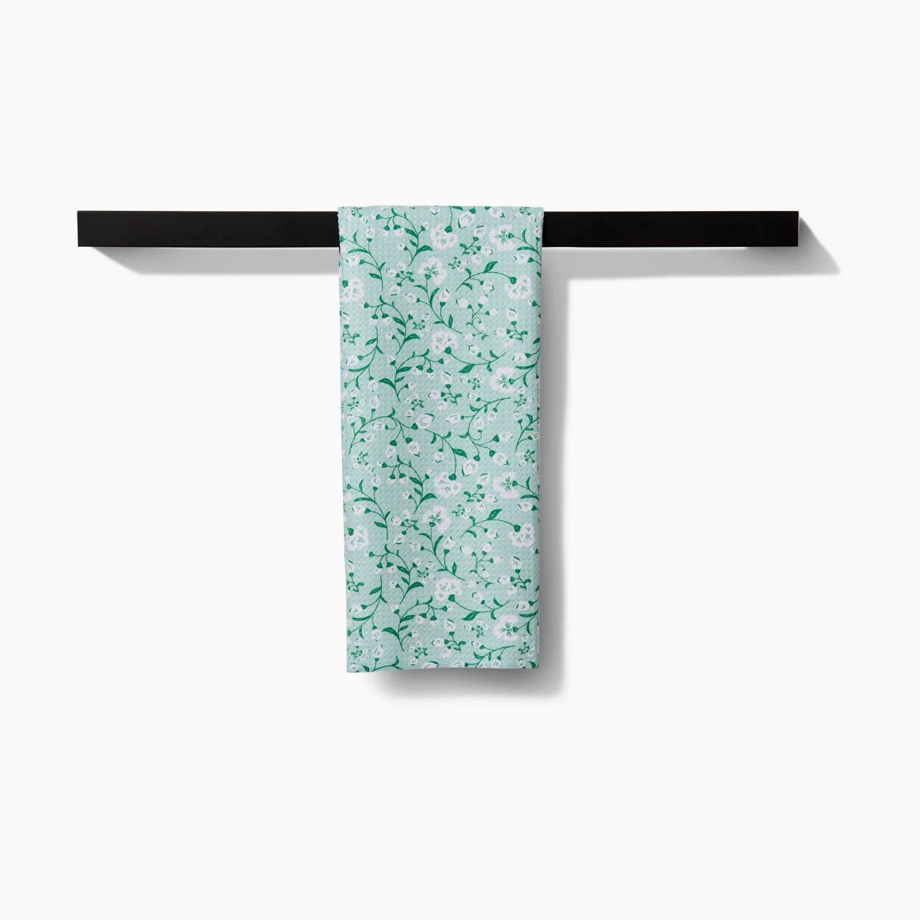 Floral-patterned towel hanging on a black towel rack against a white background Tea Towel