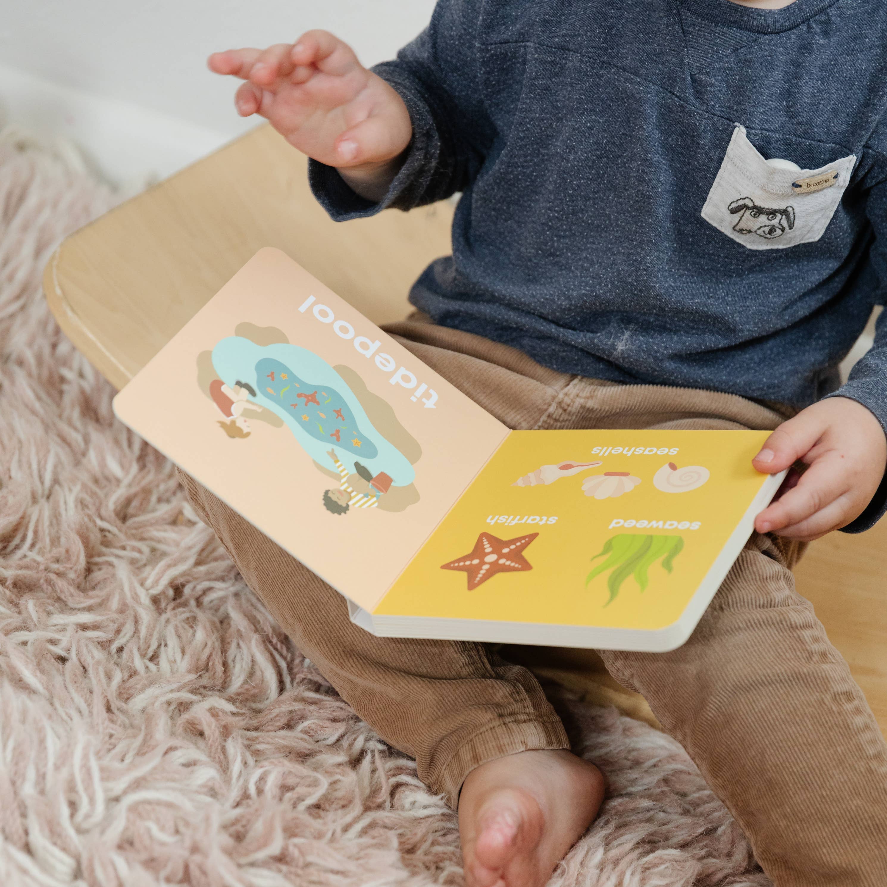 Child holding a book with animal illustrations on a fluffy pink carpet