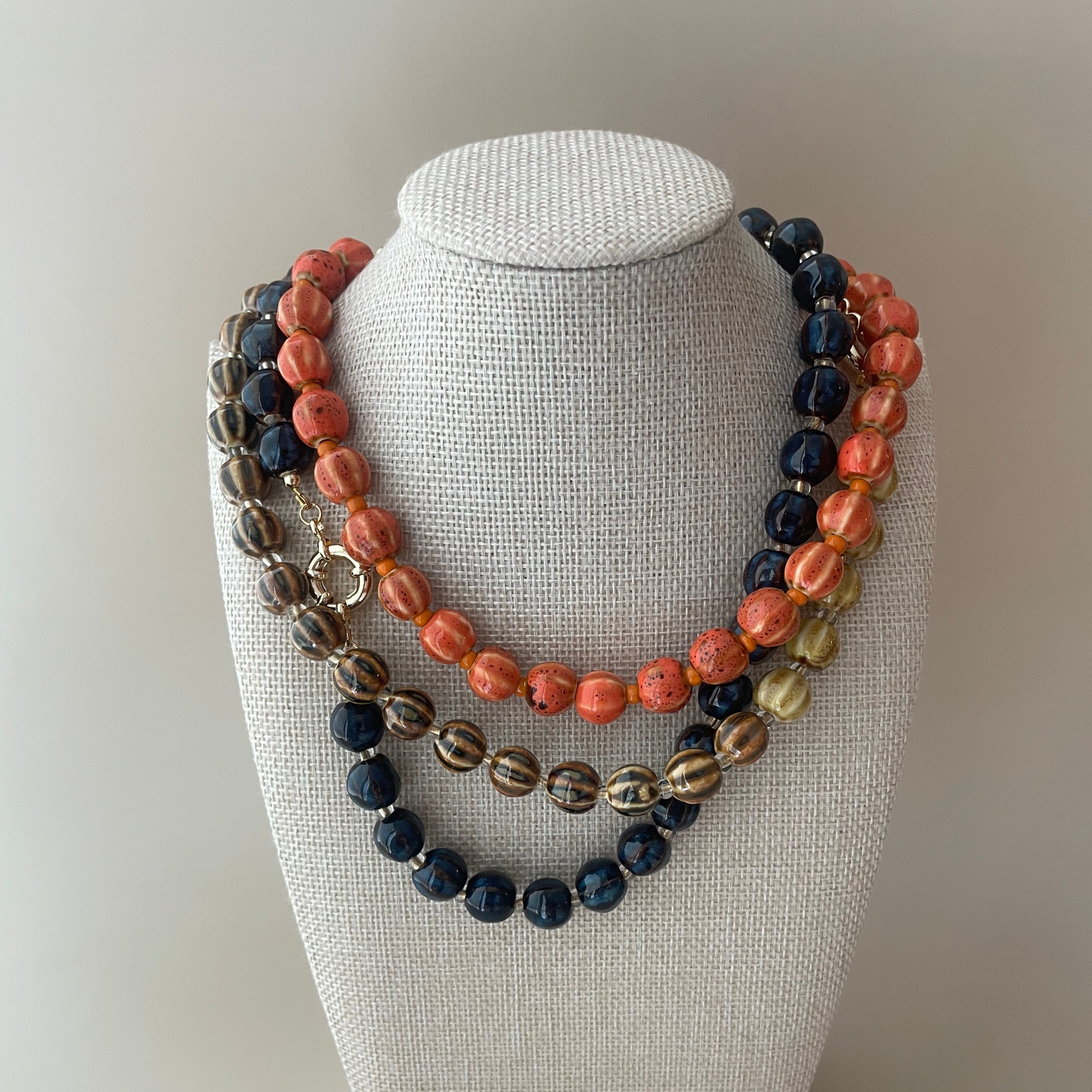 handmade ceramic beaded necklaces in various colors, with gold detail clasp