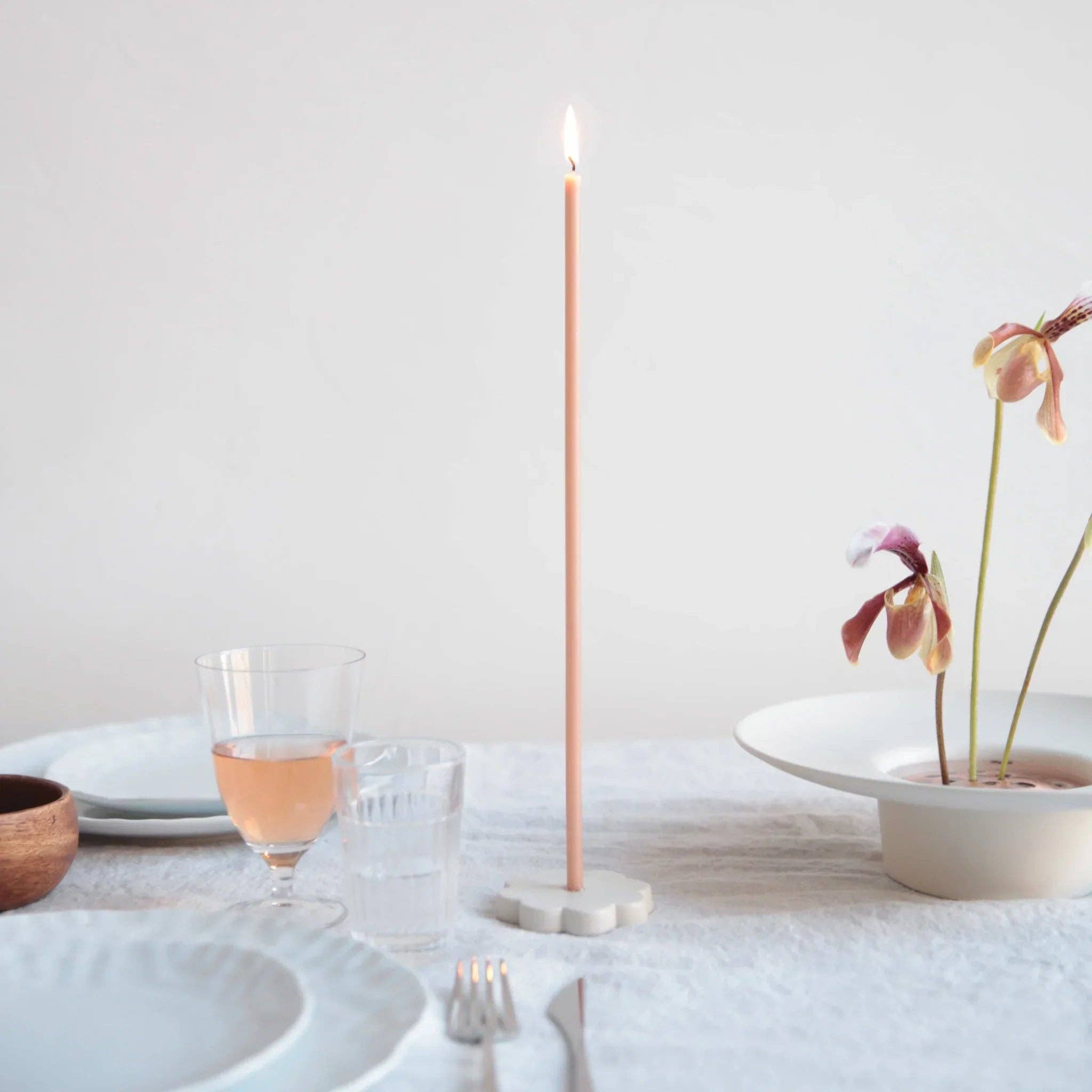 Candle on a white surface with a glass of pink wine and a potted plant.