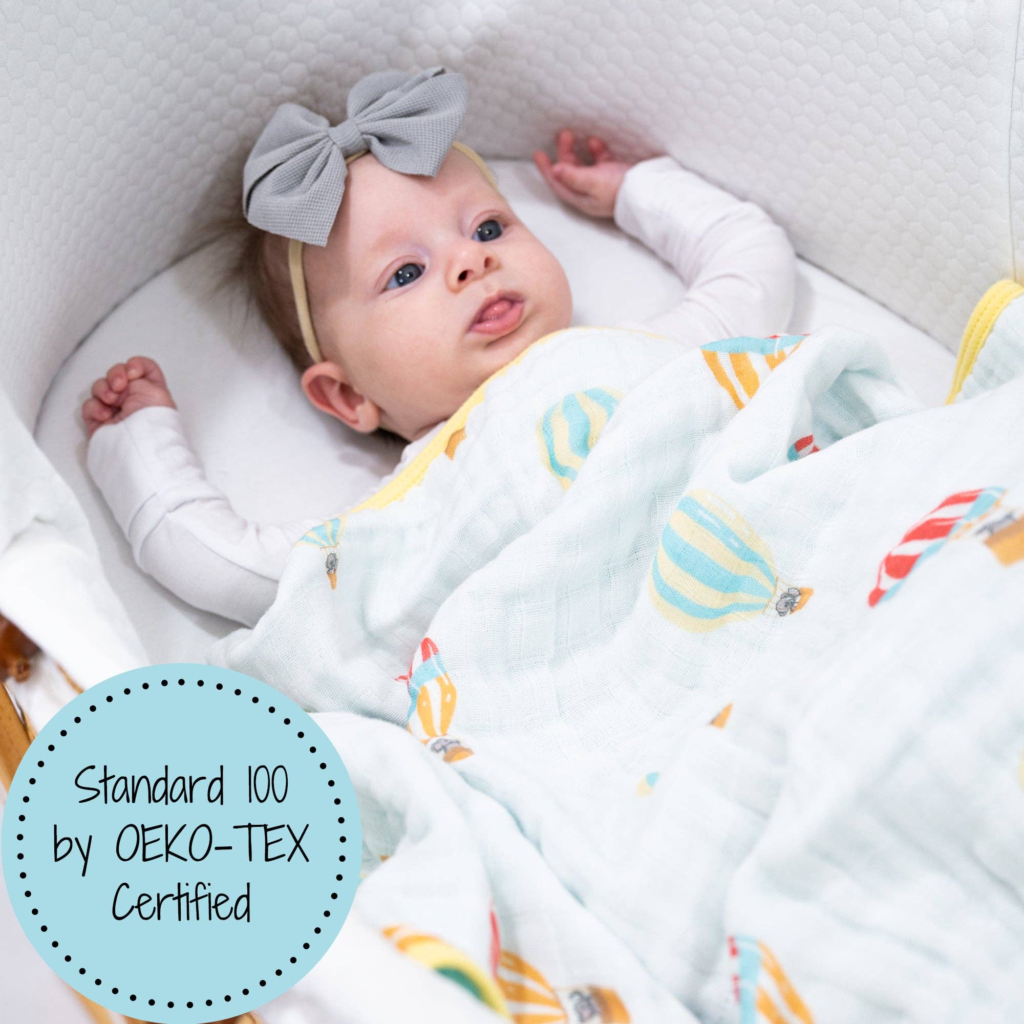 Baby lying in a crib with a colorful blanket, wearing a gray bow headband.