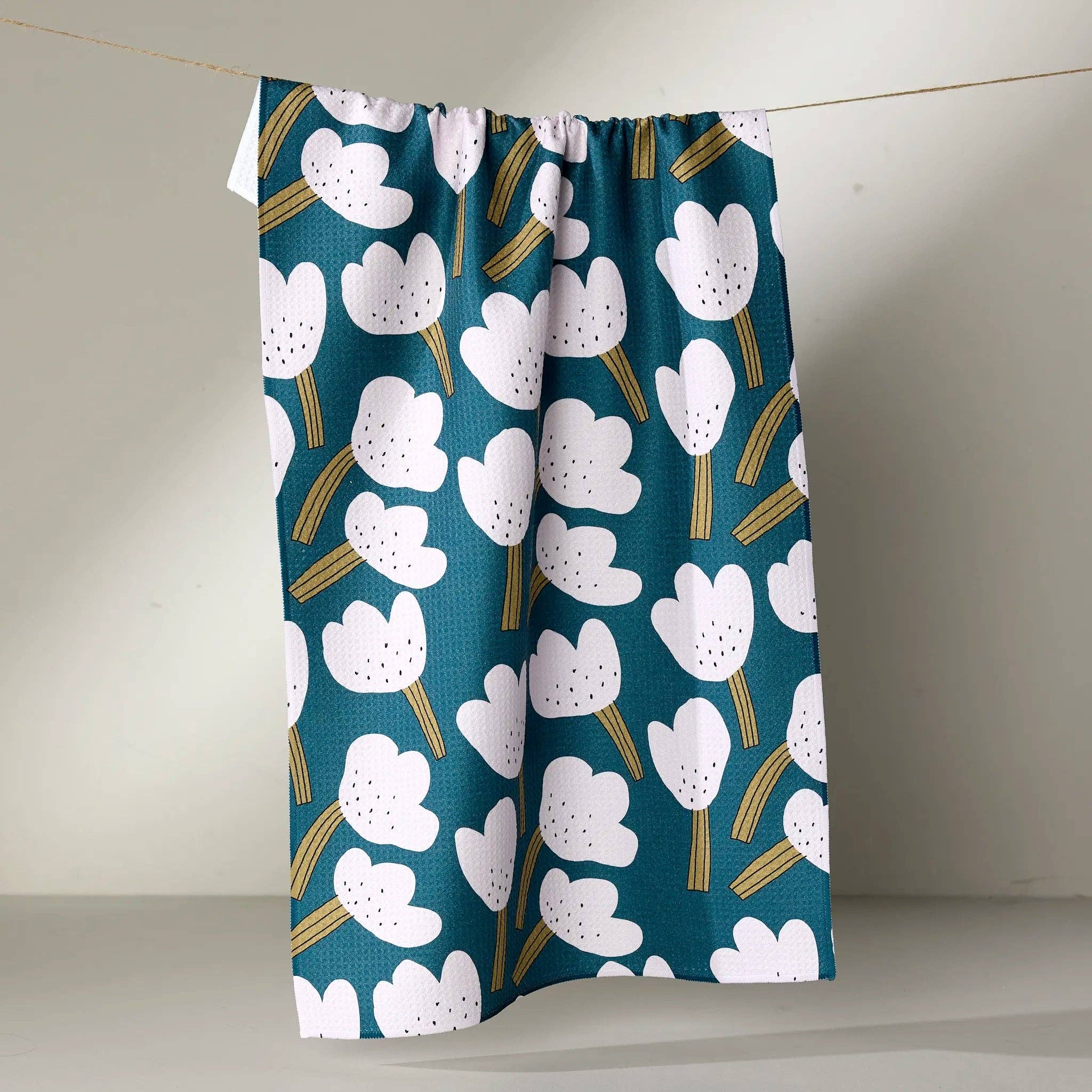 white tea towel floral pattern on a teal background hanging against a plain wall.