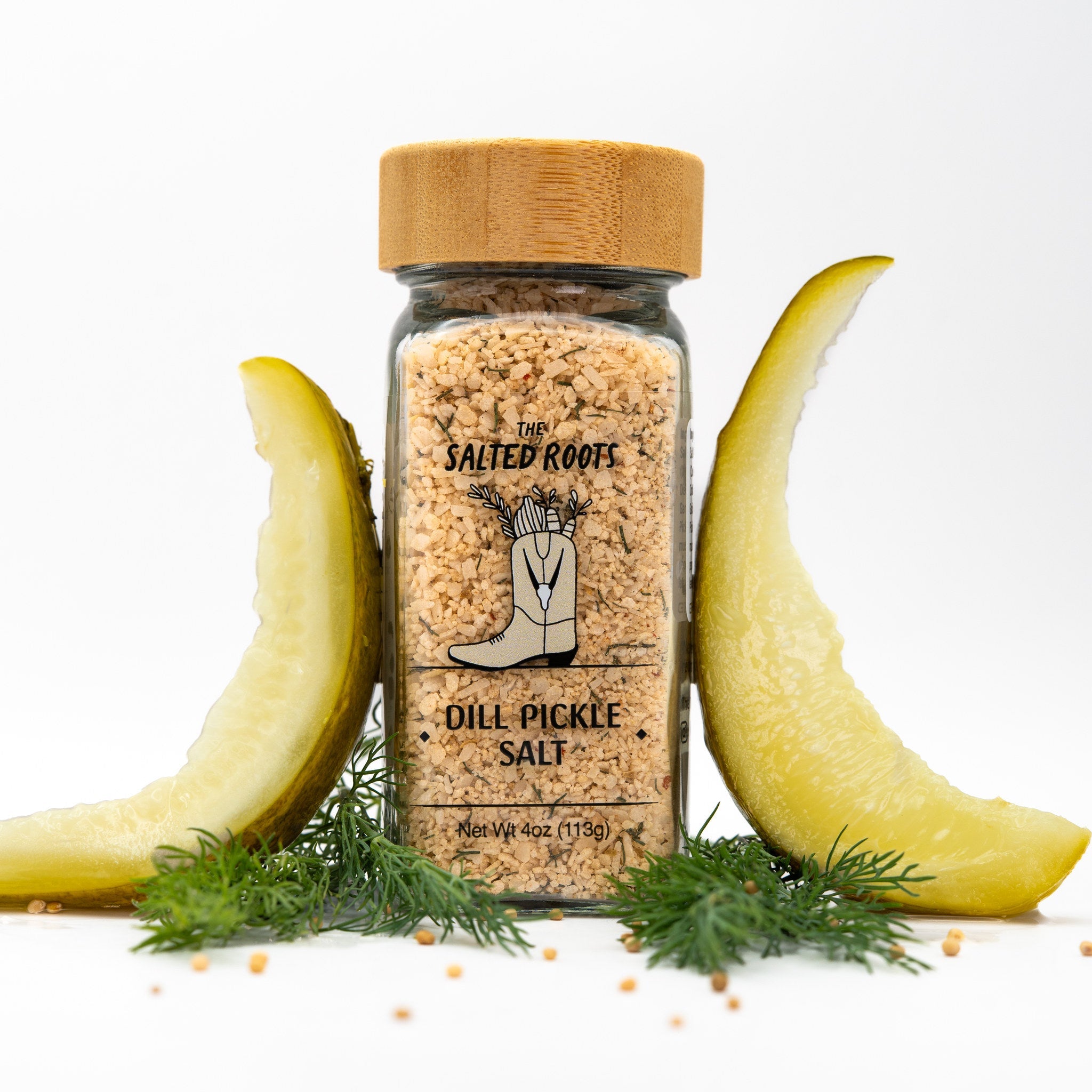 Salt jar with wooden lid and label. Dill pickle spears and dill fronds arranged around jar.