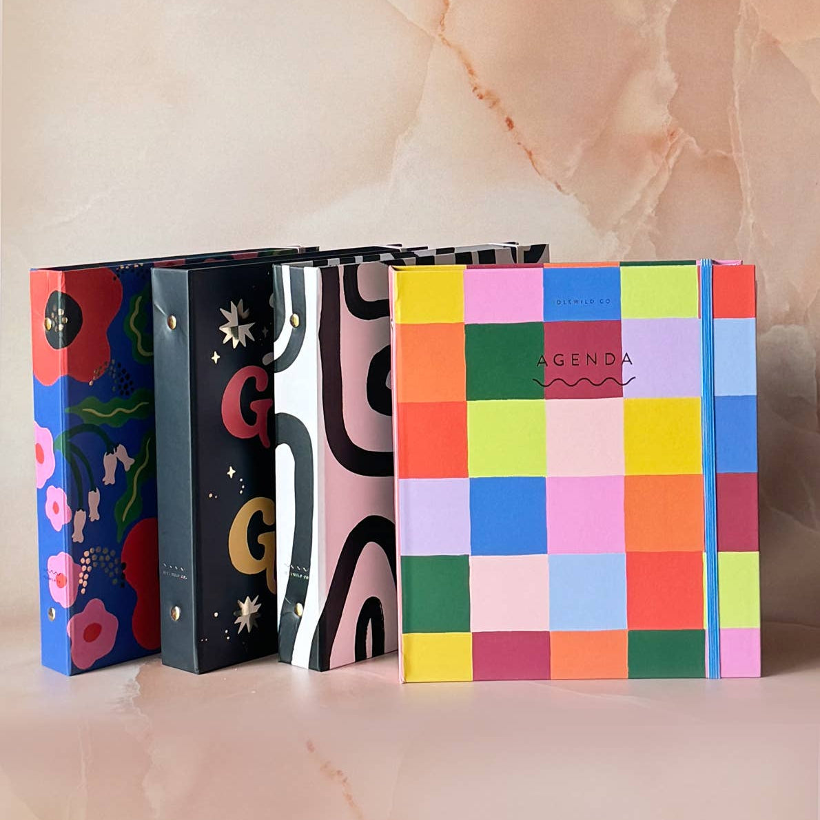 Four colorful notebooks with different designs on a soft pink background