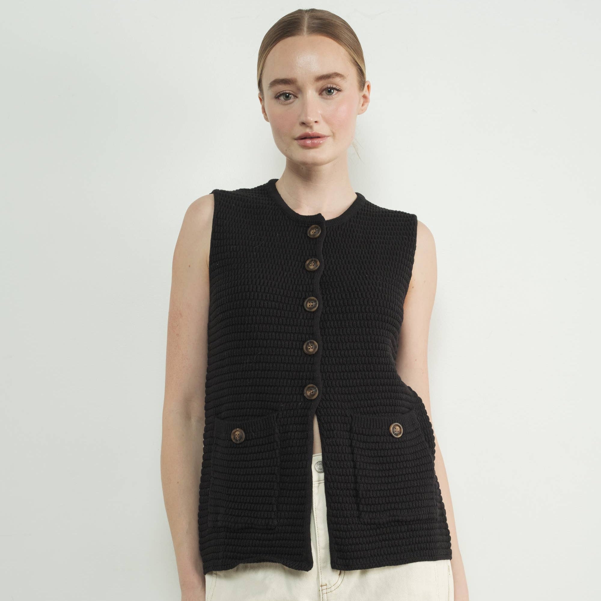 This black sweater vest is the epitome of cozy-chic style, featuring allover ribbed texture and classic button-up closure for a refined yet modern aesthetic. Designed for versatility, it can be worn as a standalone statement. Fitted silhouette that beautifully enhances femininity and complements any outfit. 