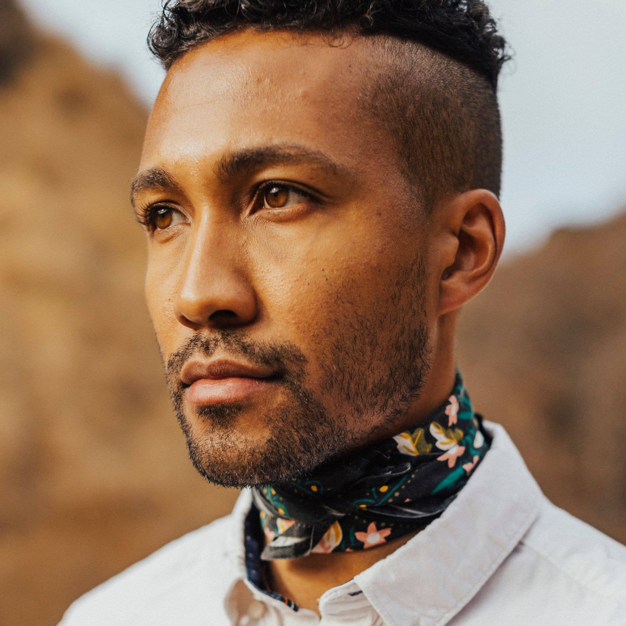 Man wearing a white shirt and floral neck scarf with a blurred natural background
