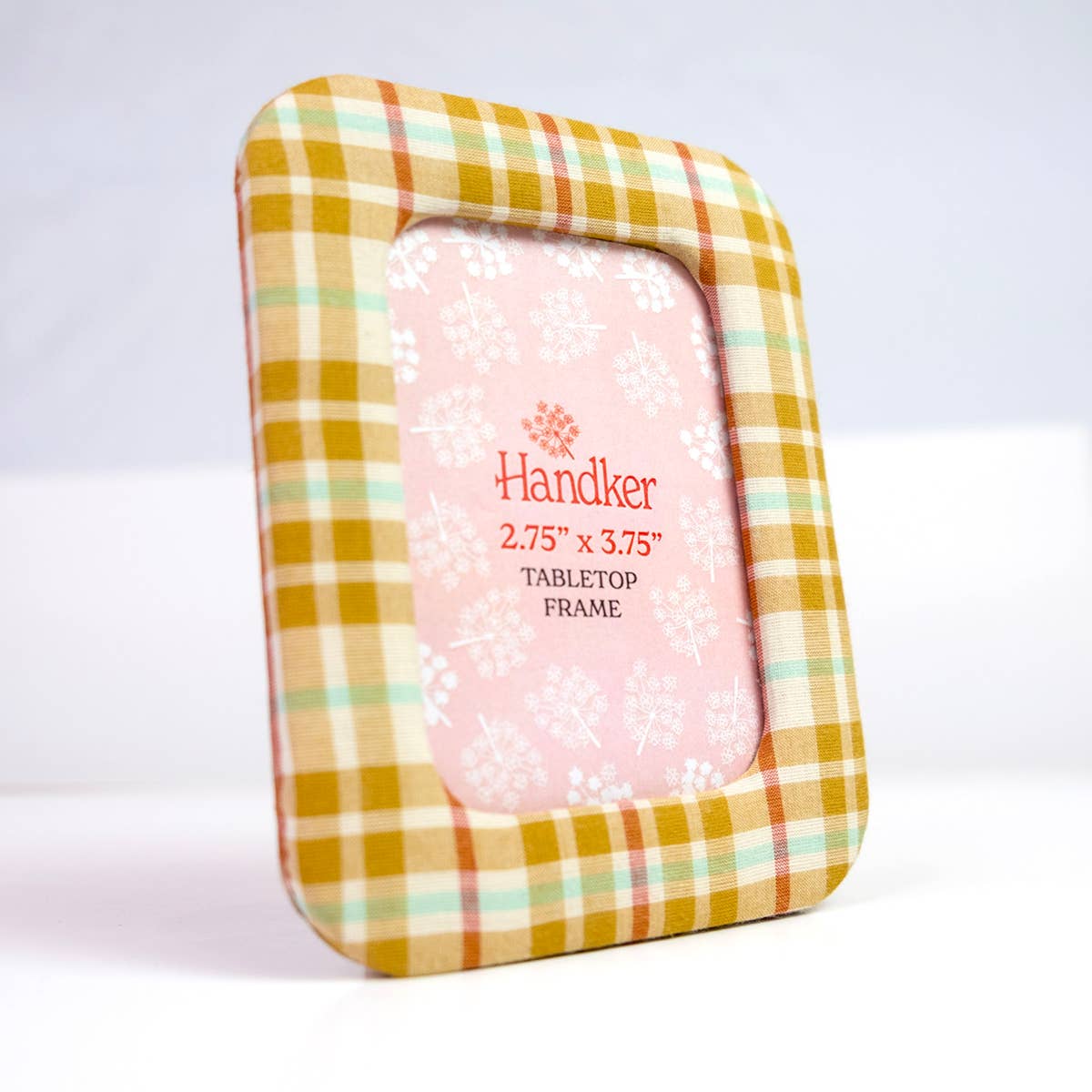 A small rectangular tabletop picture frame with a mustard yellow, beige, and mint green plaid border, holding a pink patterned insert card. The card is printed with the brand name 'Handker' and size information.