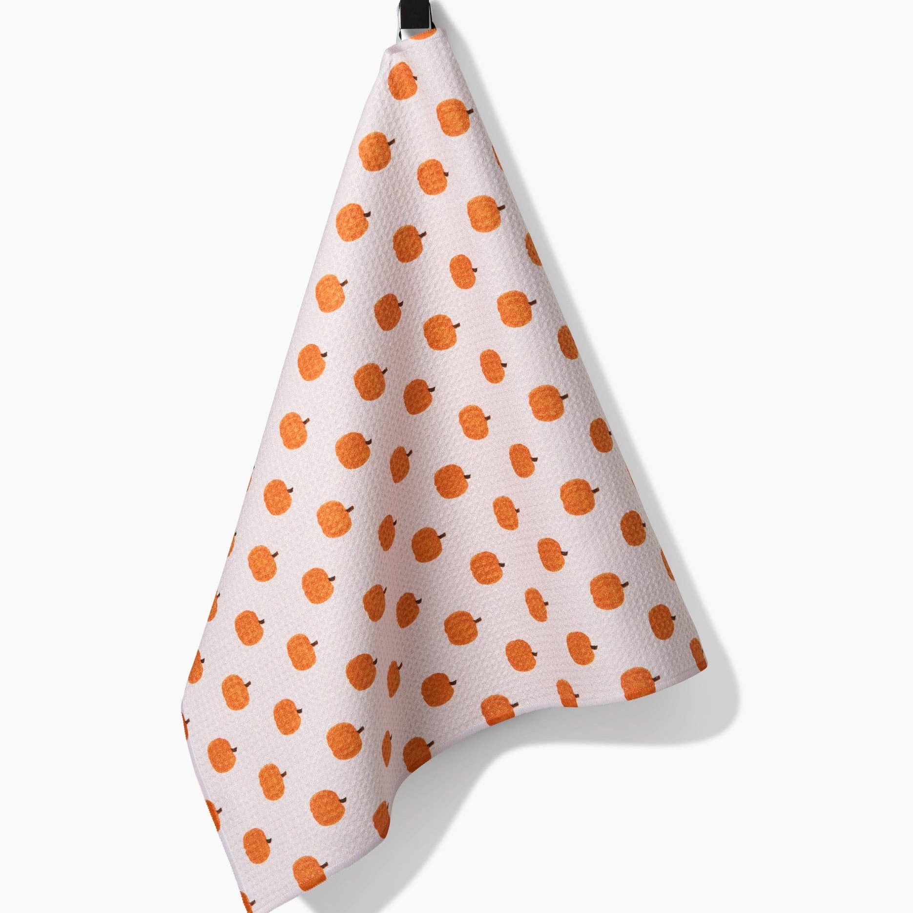 White towel with orange pumpkin pattern hanging on a black hook against a white background