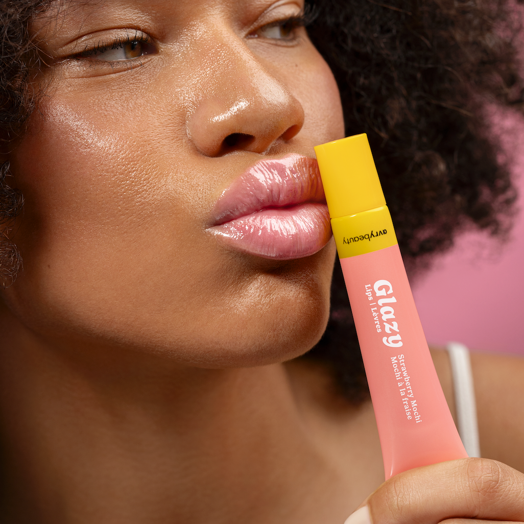 Woman holding a pink lip gloss with a yellow cap against a blurred background