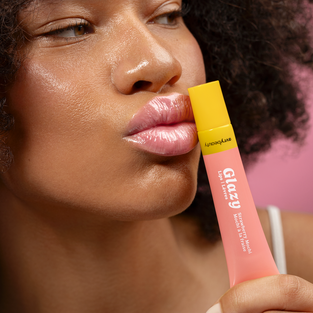 Woman holding a pink lip gloss with a yellow cap against a blurred background