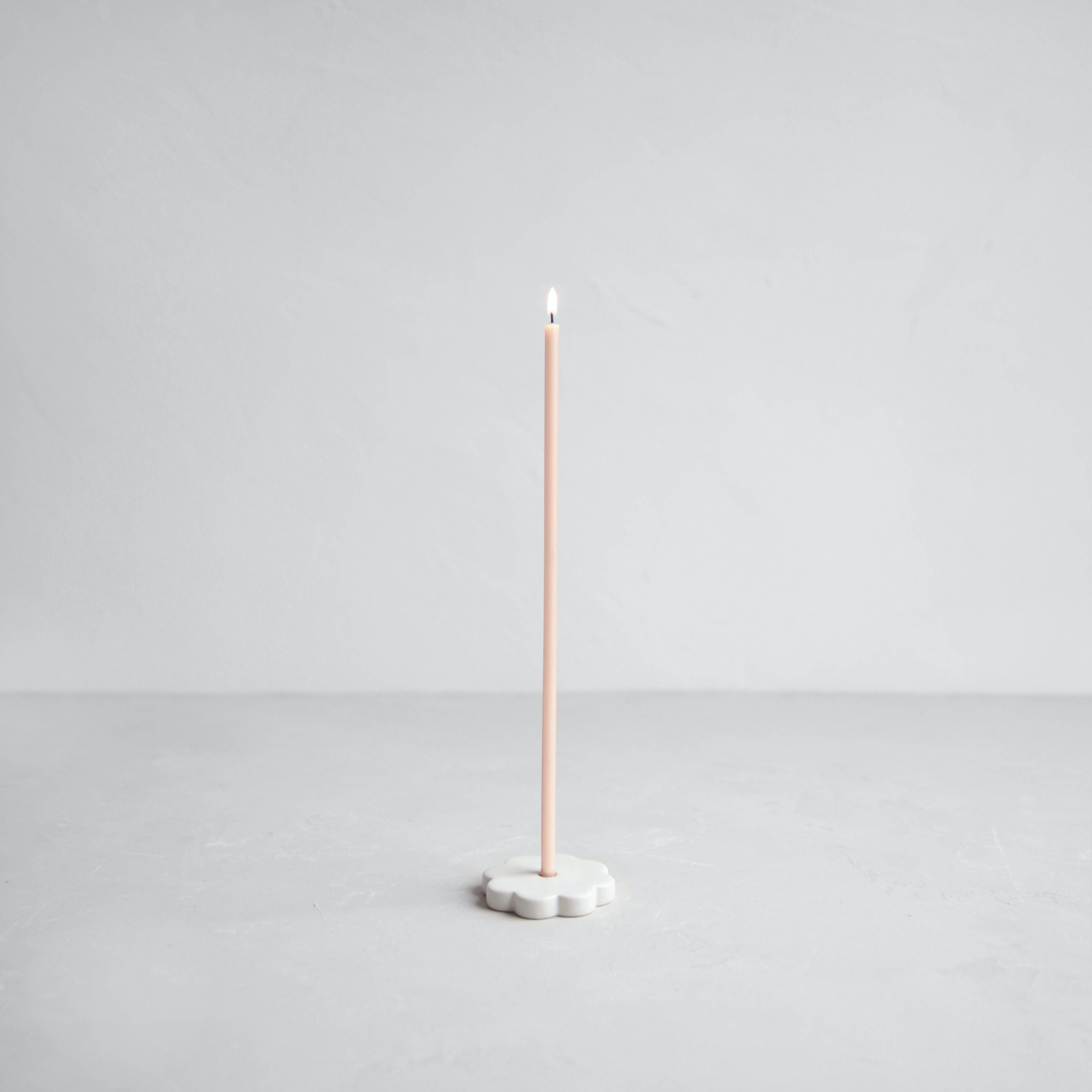 Tall candle on a white base against a light gray background