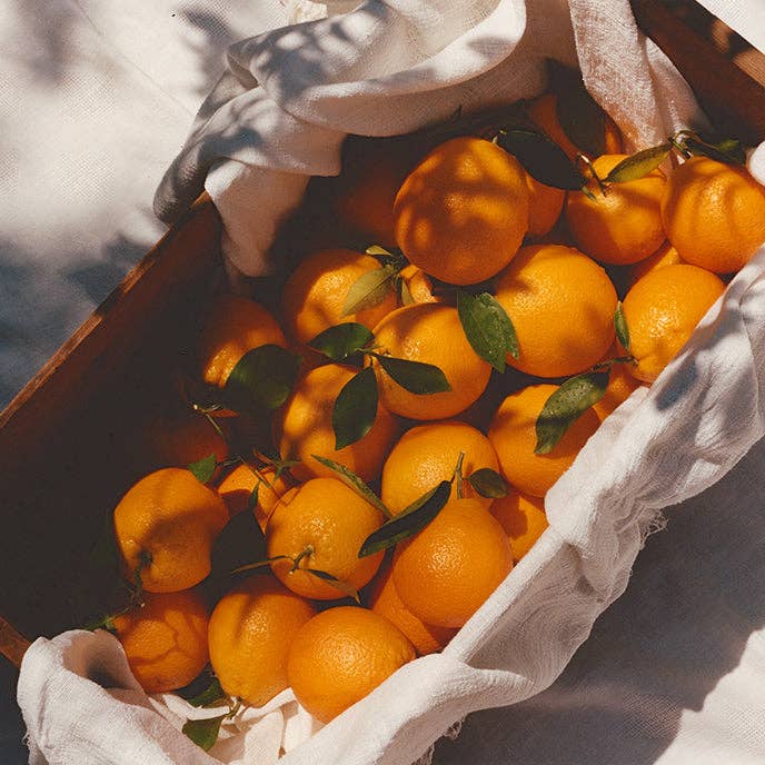 Oranges with leaves in a wooden box lined with white fabric
