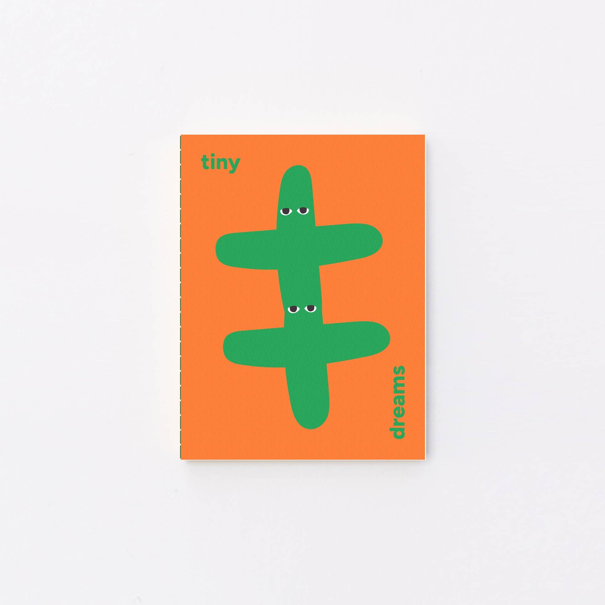 A small notebook or book cover with an orange background and a green abstract character illustration, photographed against a clean white background.
