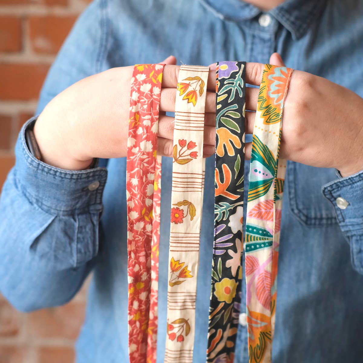 Person holding four colorful fabric straps with floral patterns against a brick wall.