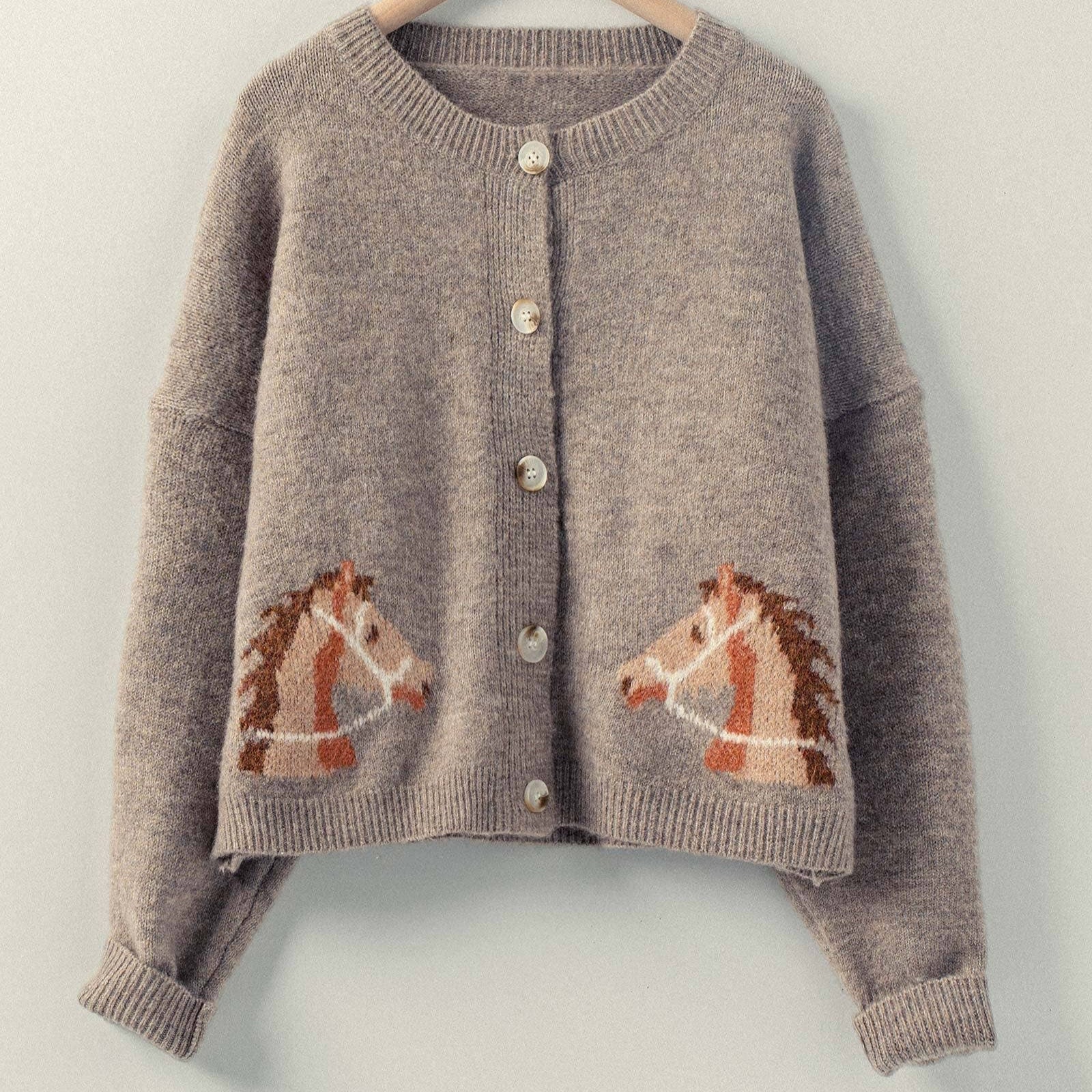 Mocha knitted cardigan with horse designs on a hanger against a light background