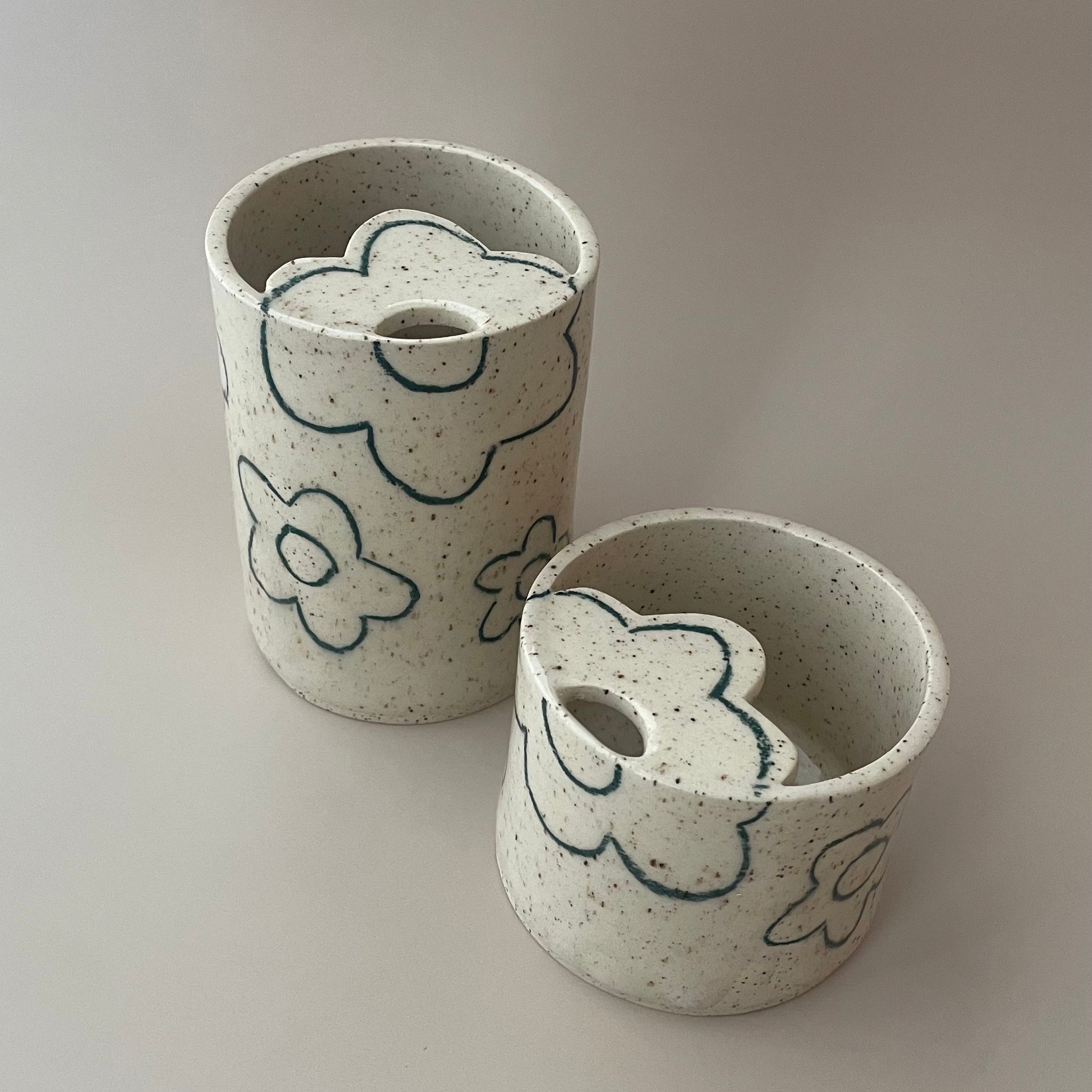 ceramic travel cup with a beige speckled glaze and dark green flower details, featuring a flower shaped lid with a sip hole