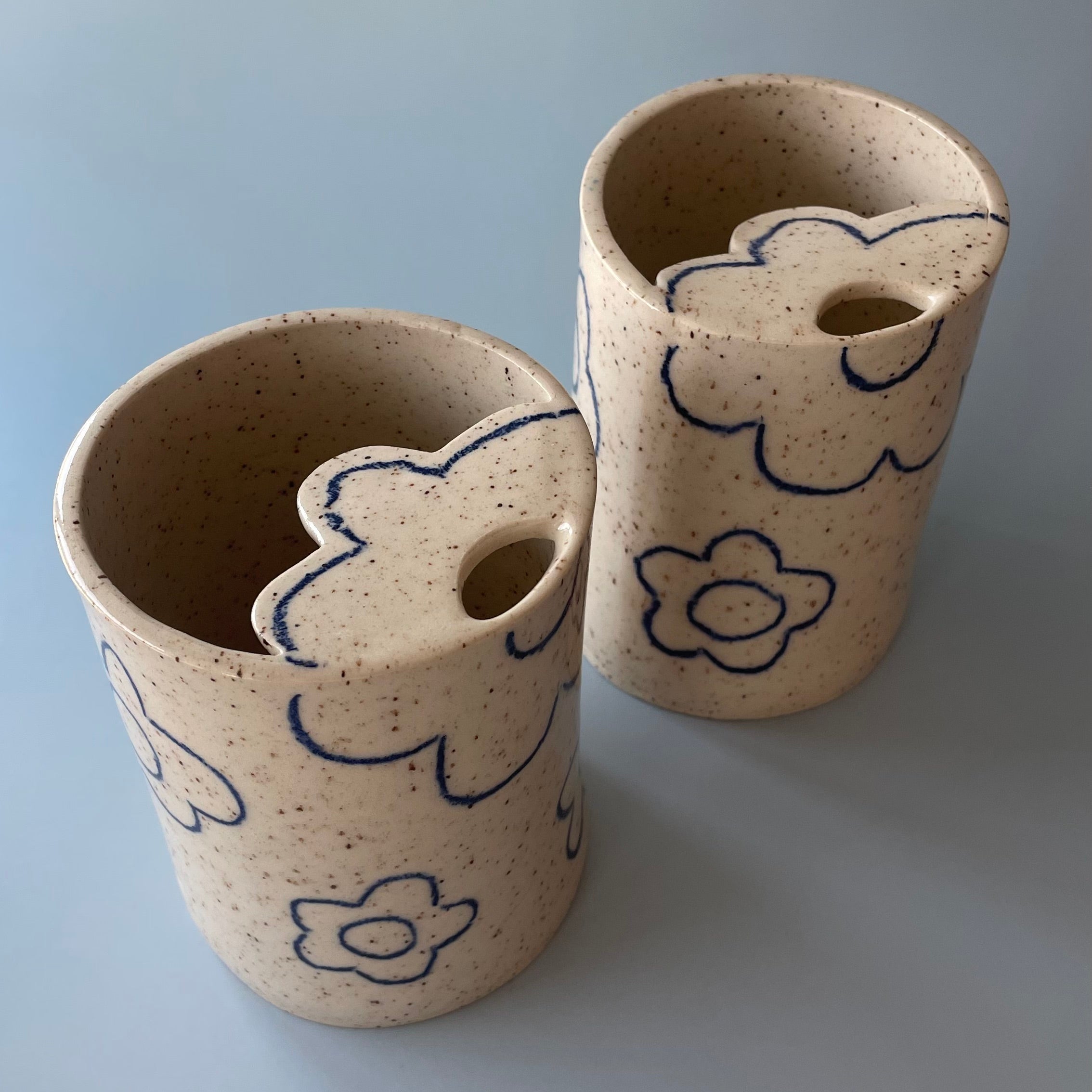 ceramic travel cup with a beige speckled glaze and dark blue flower details, featuring a flower shaped lid with a sip hole