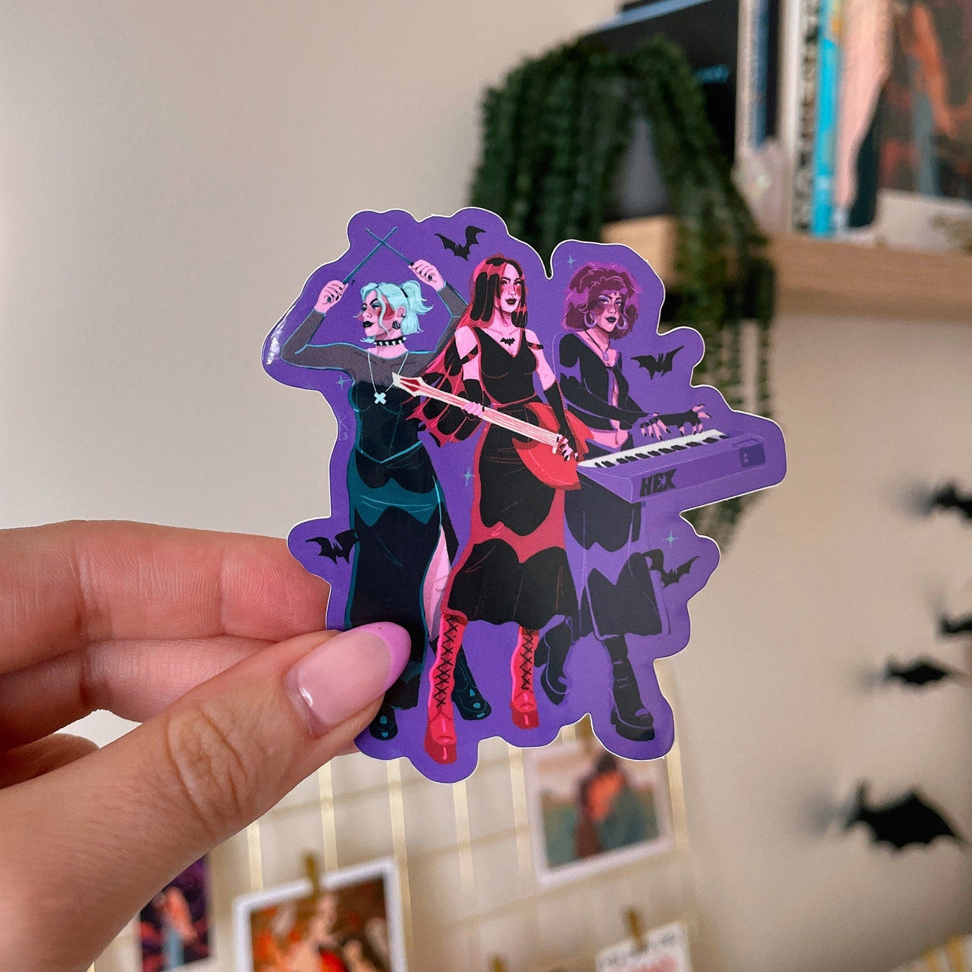 a hand holding a purple sticker featuring artwork of the three hex girls from Scooby-Do