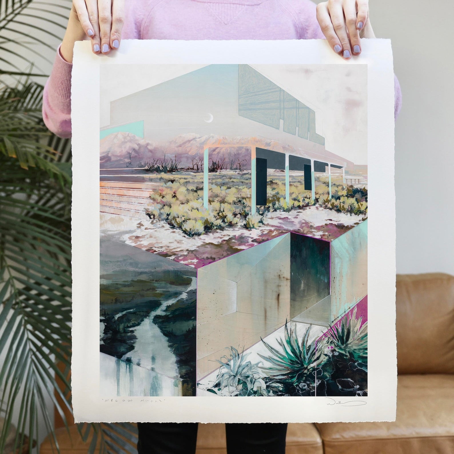 print held by woman against leather couch and fern.