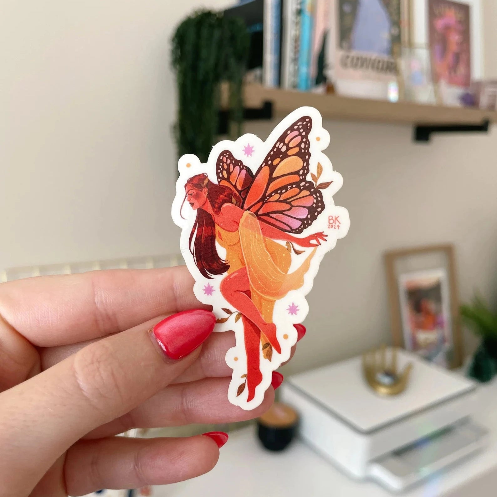 This sticker has a glossy vinyl finish and a clear back once taken off the backing paper. A woman wearing a pale yellow dress has large monarch wings attached to her.