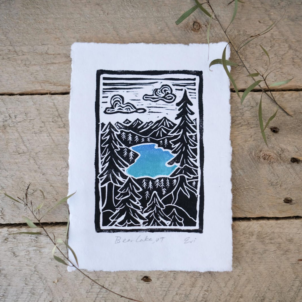 Black and white linocut print of bear lake with blue water