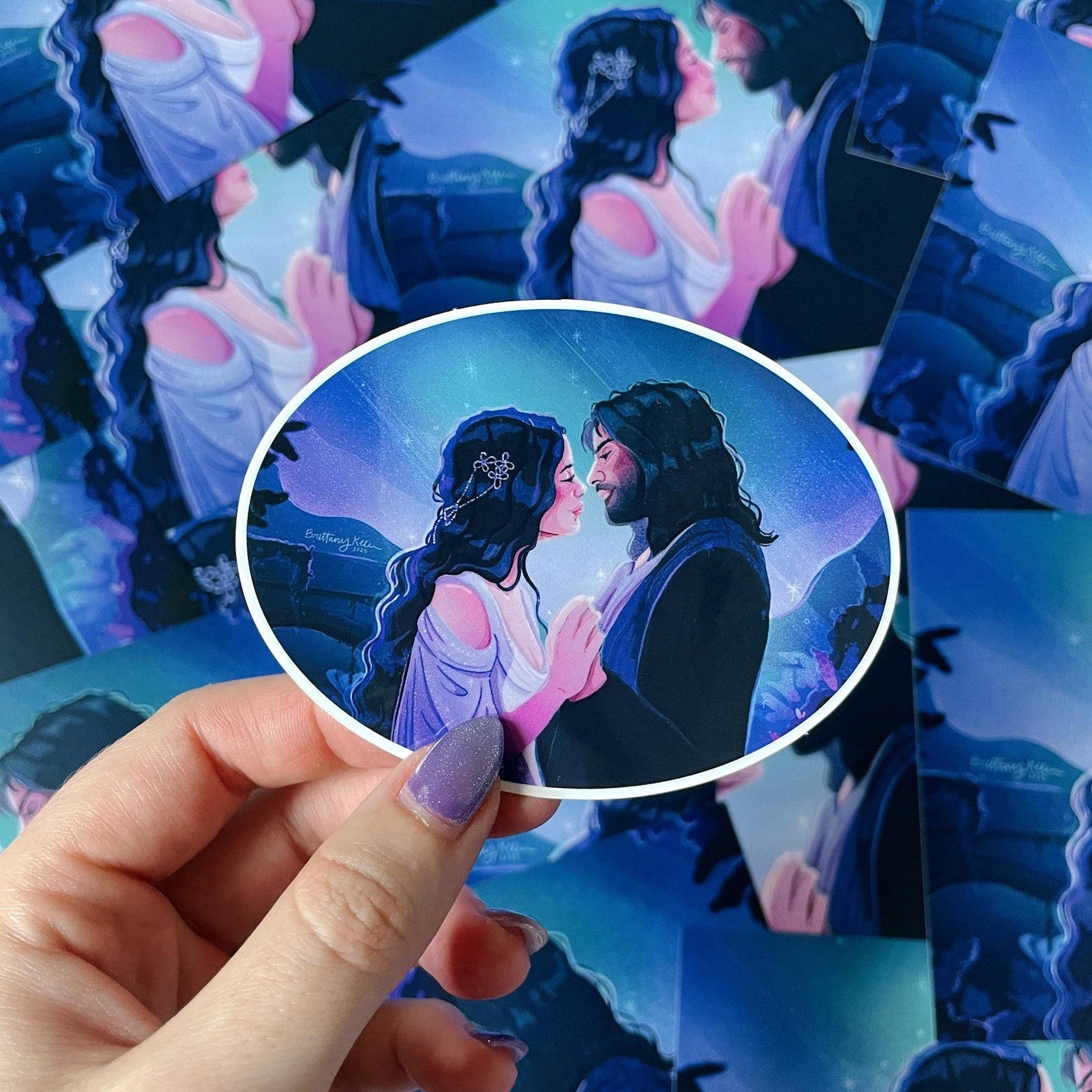 a hand holding a sticker featuring a man and woman holding hands looking at each other lovingly with a blue and purple starry scene behind them