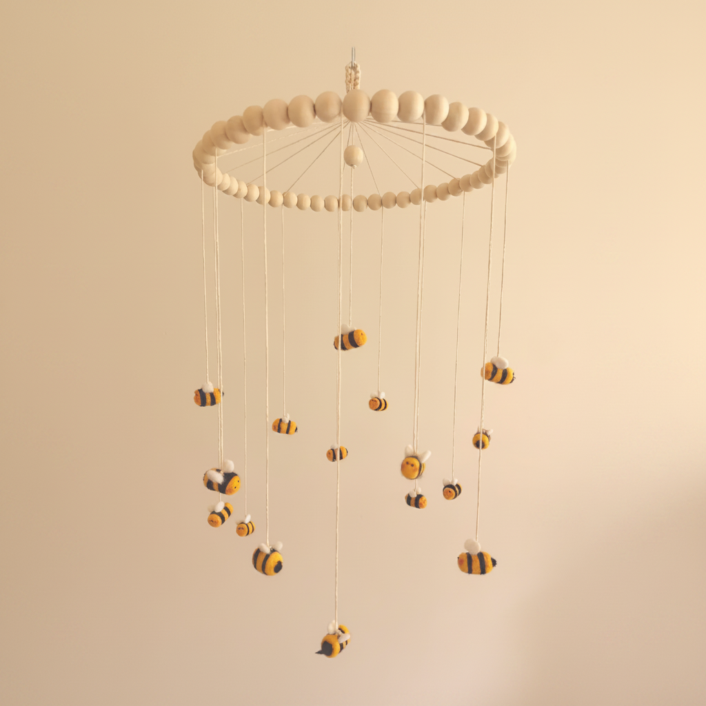 A handcrafted wool baby mobile featuring soft, felted bumble bees suspended from natural wood and cotton cord. The gentle, colorful design moves delicately above the crib, inviting visual exploration and discovery. Each bee is carefully crafted from natural materials to inspire wonder while supporting early visual development