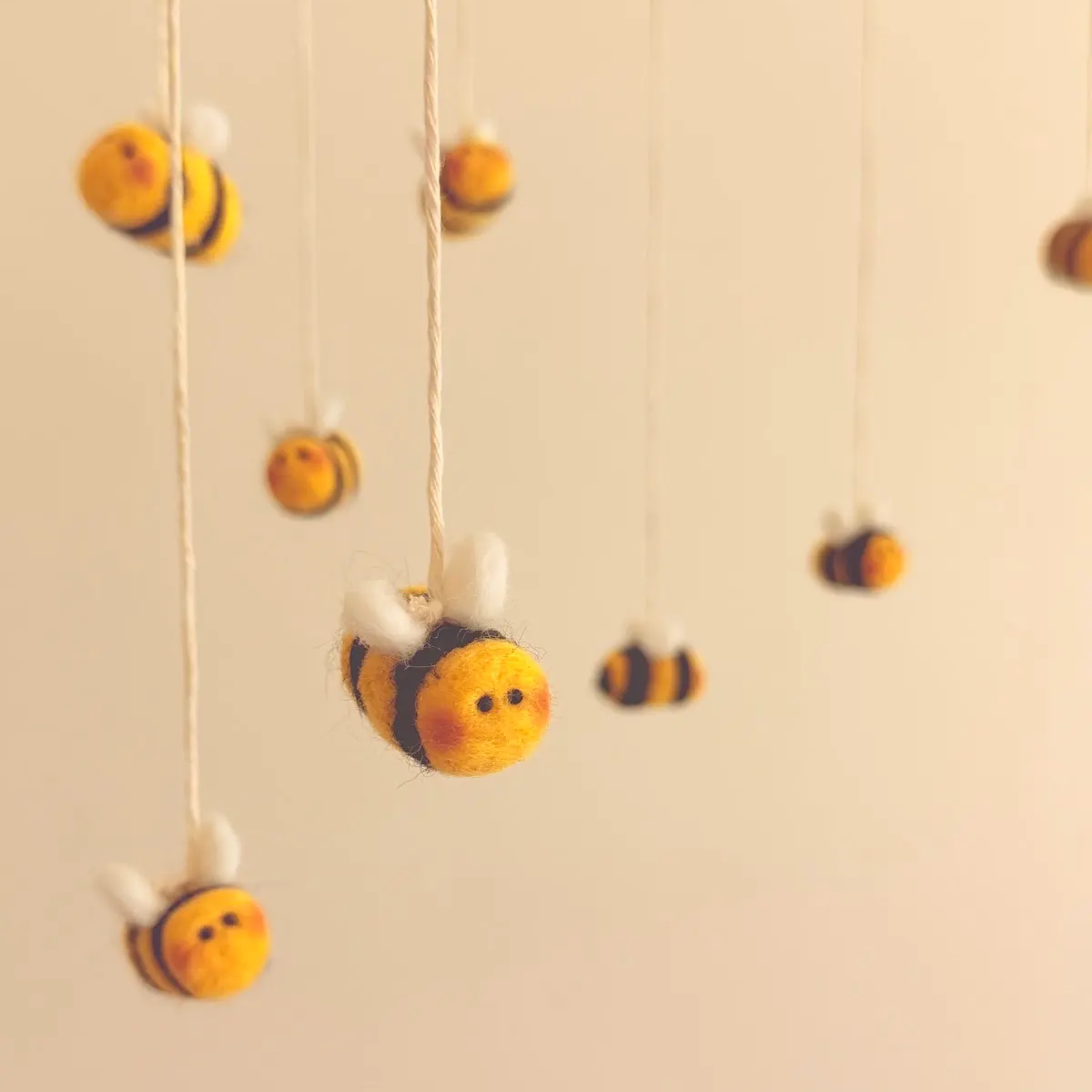 A handcrafted wool baby mobile featuring soft, felted bumble bees suspended from natural wood and cotton cord. The gentle, colorful design moves delicately above the crib, inviting visual exploration and discovery. Each bee is carefully crafted from natural materials to inspire wonder while supporting early visual development