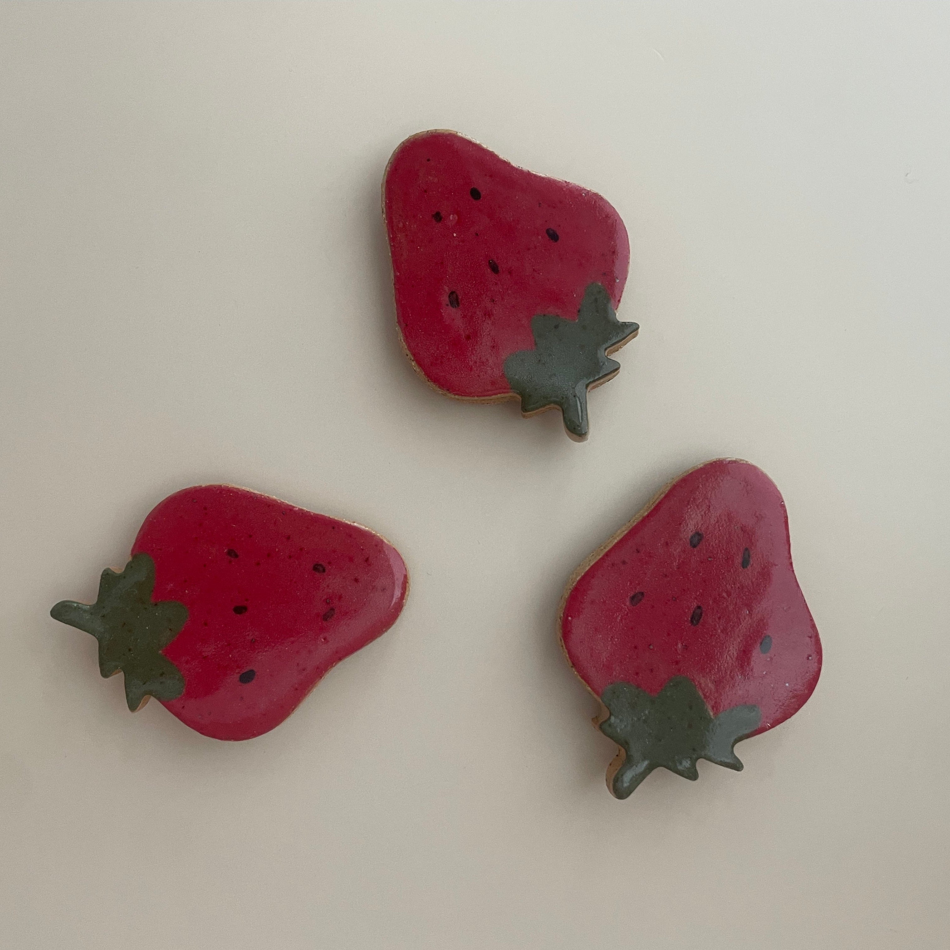 flat ceramic strawberry magnet with a red glazed base, black seed details, and green on top