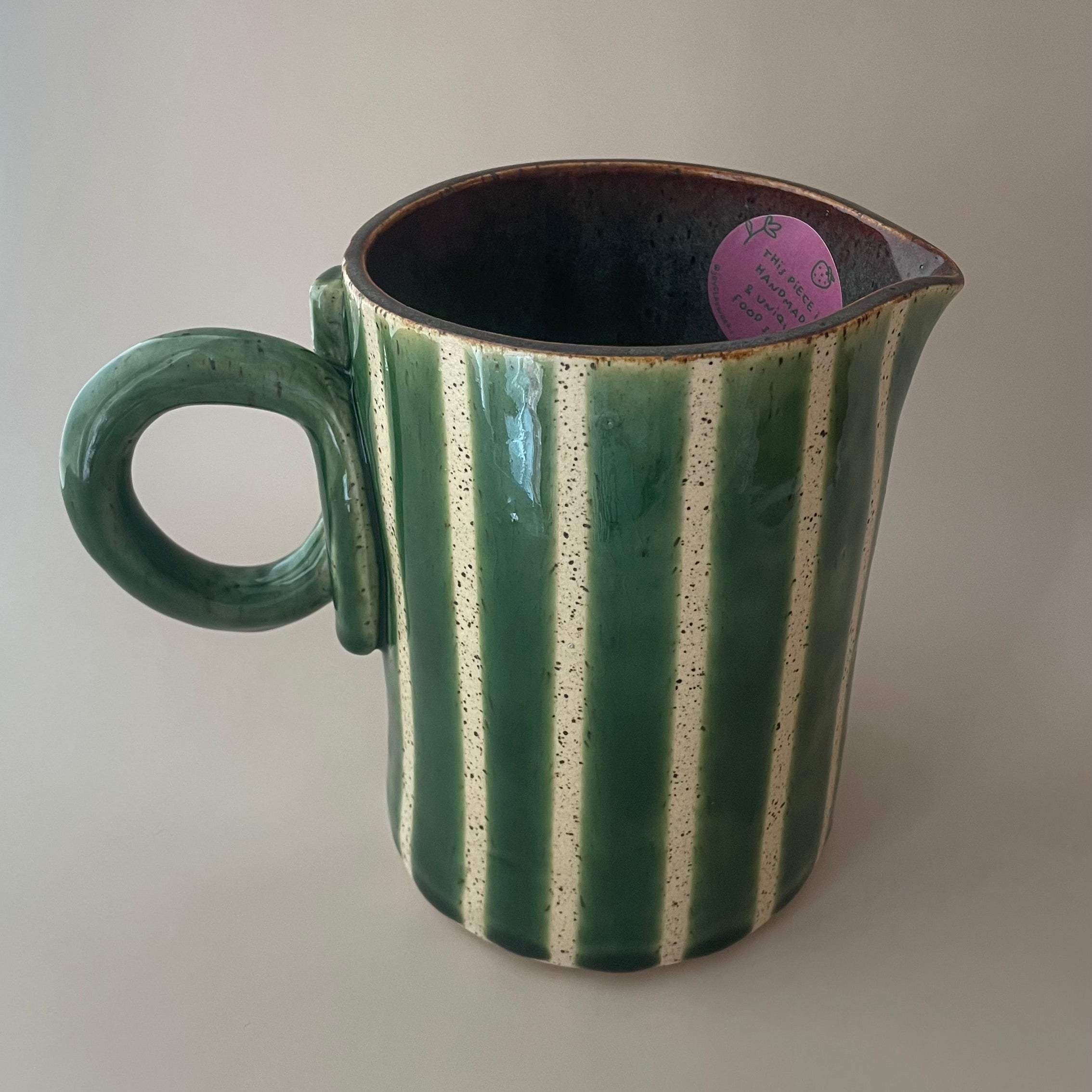 handmade ceramic pitcher with beige base, green stripes, dark blue/purple glaze inside, and a green looped handle design